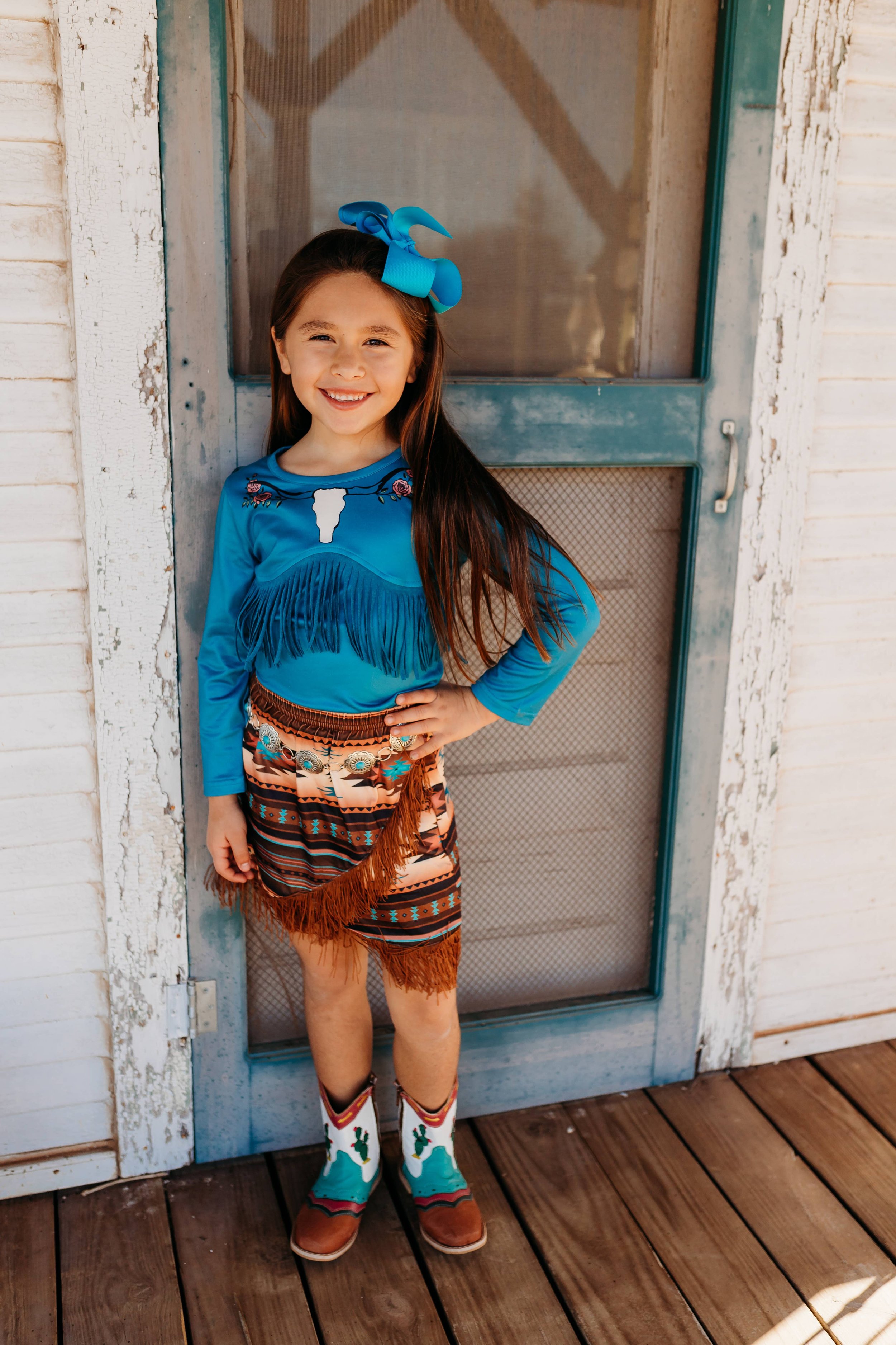 Young girl wearing a blue fringed western outfit and cowboy boots.