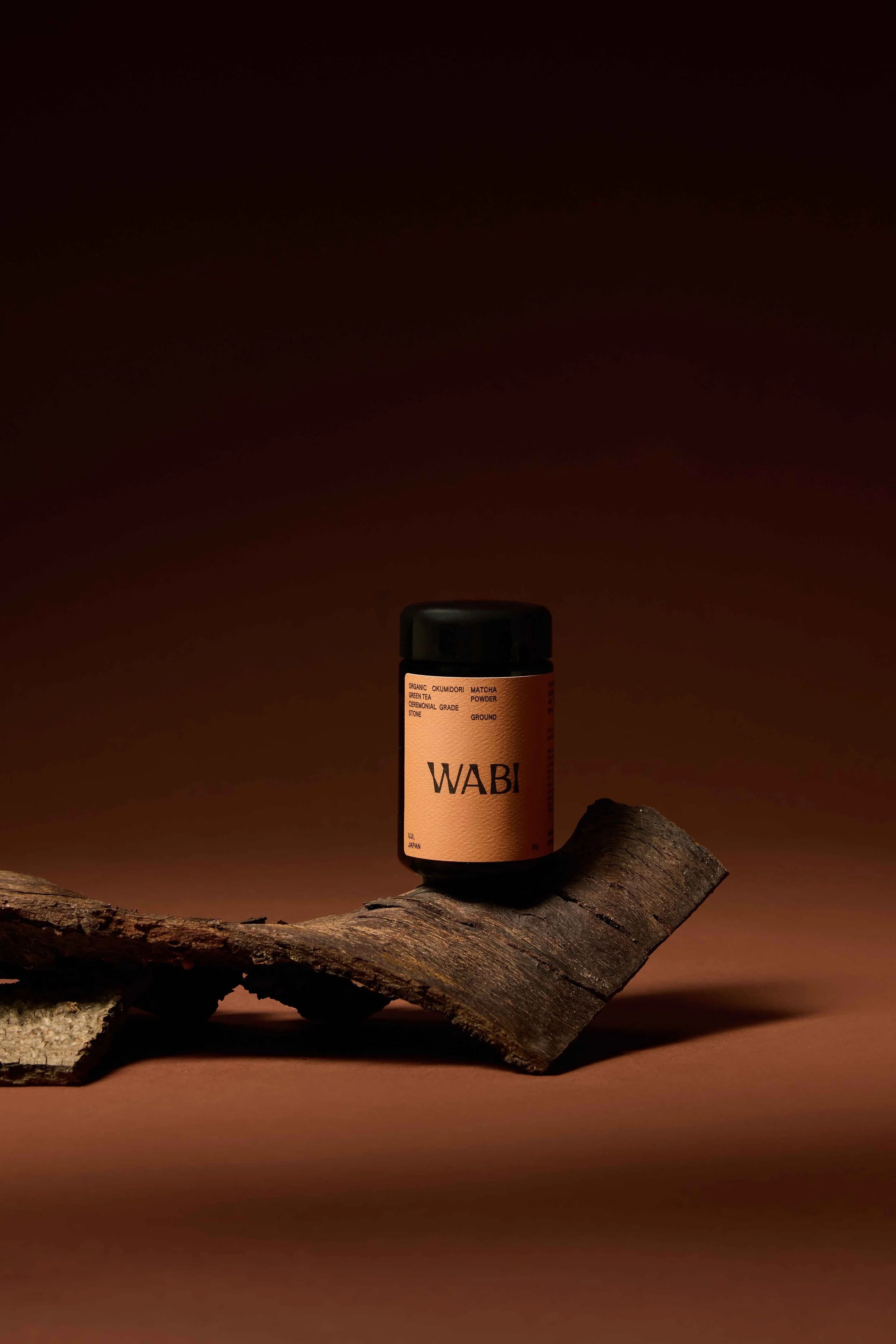 A small container labeled 'WABI' placed on a piece of wood, with a brown background.