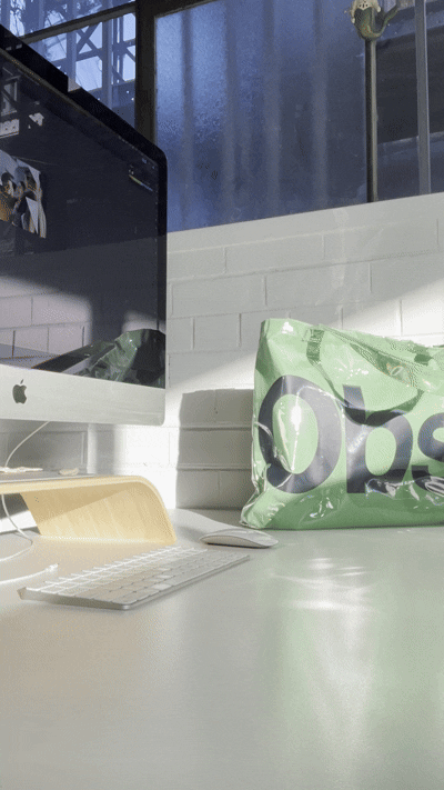 A workspace with an iMac computer, a keyboard, a mouse, and an OXXO shopping bag on a white desk in front of a white brick wall.