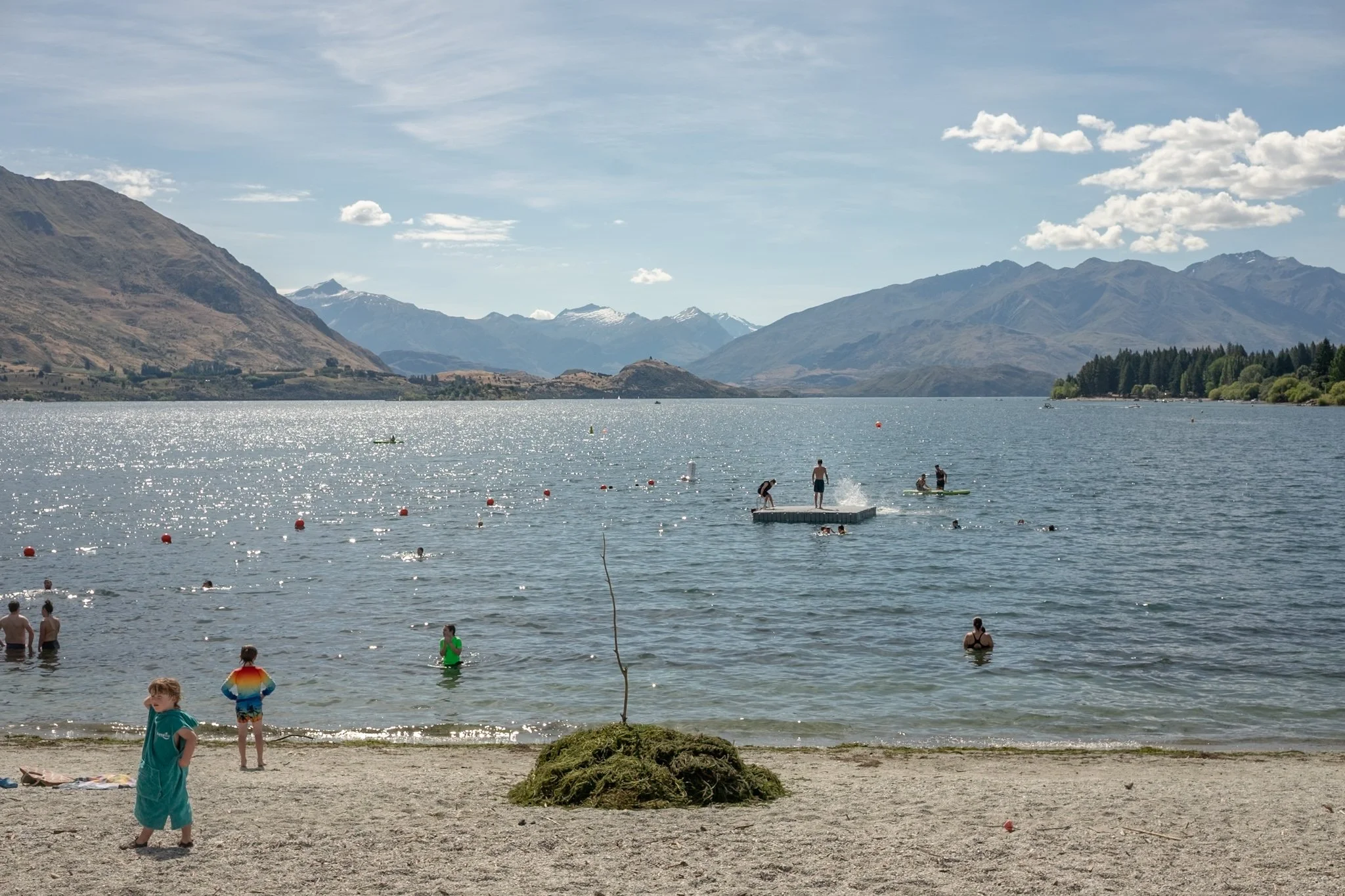 People swimming and enjoying a day at a lake with mountainous landscape in the background.
