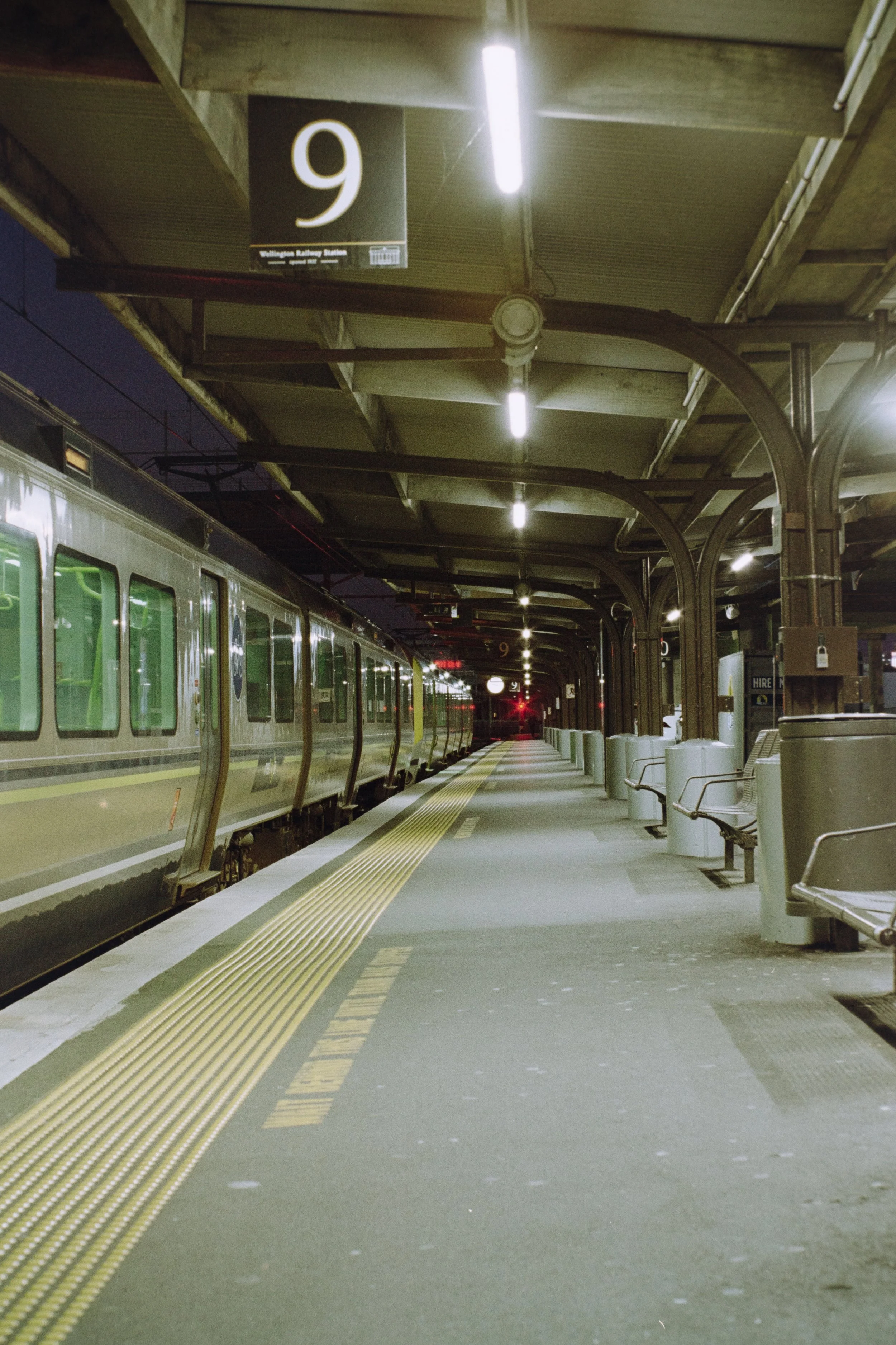 Nighttime at Wellington Railway Station in New Zealand with an empty platform, benches, and a train on the left side.
