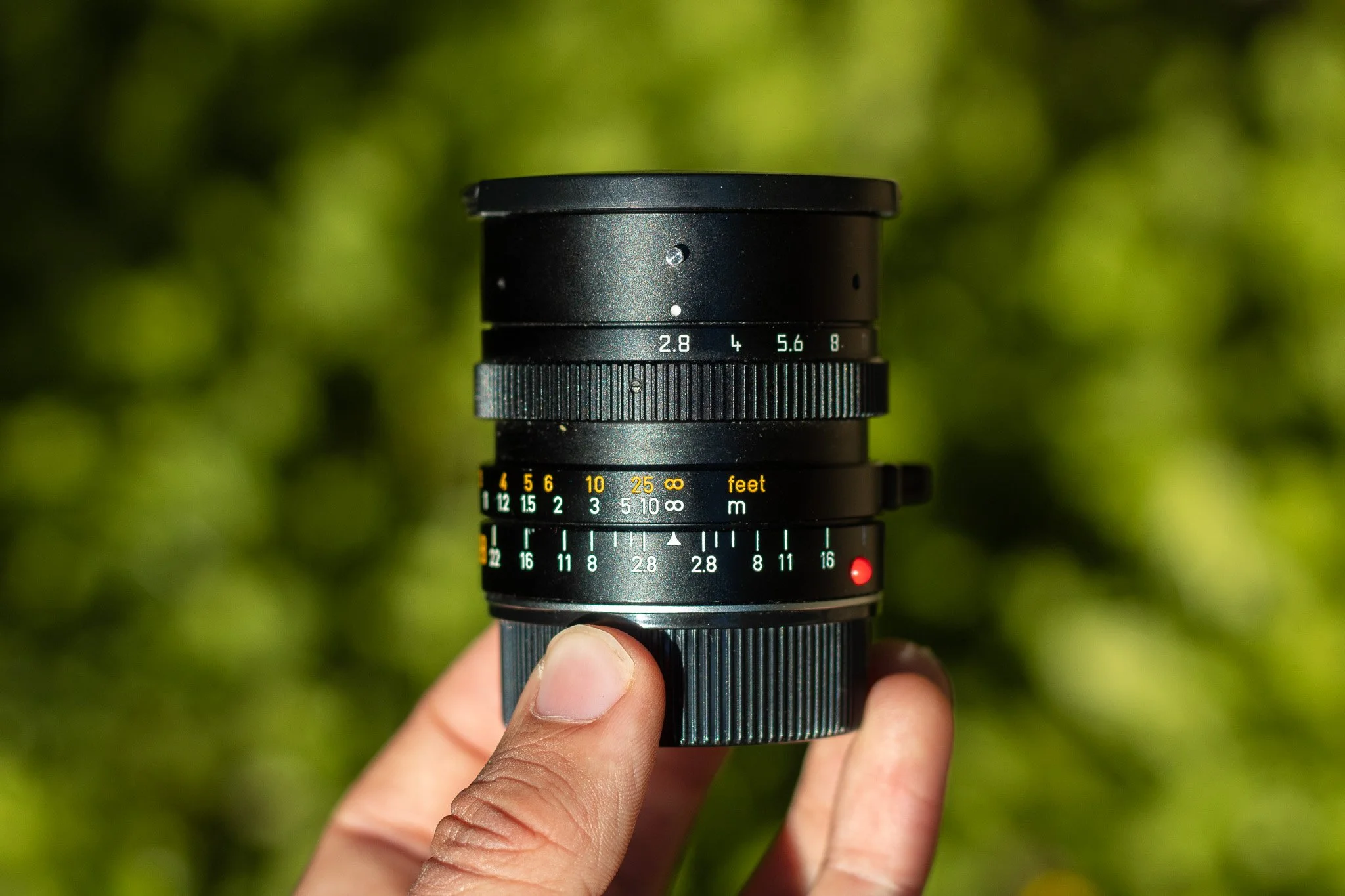 Close-up of a professional camera lens being held by a person's hand against a blurred green background.