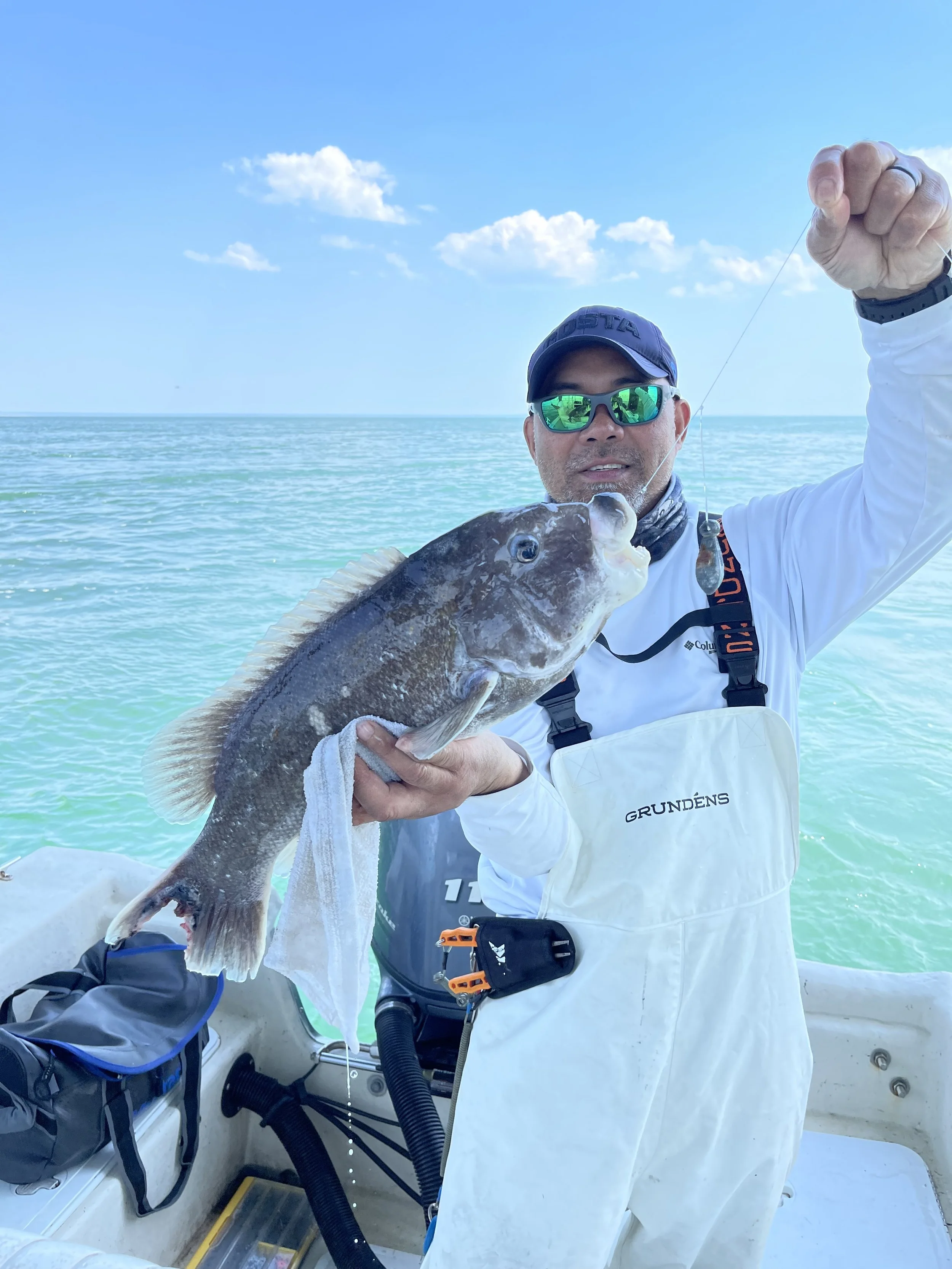 Man on boat holding a large fish with water and sky in the background.