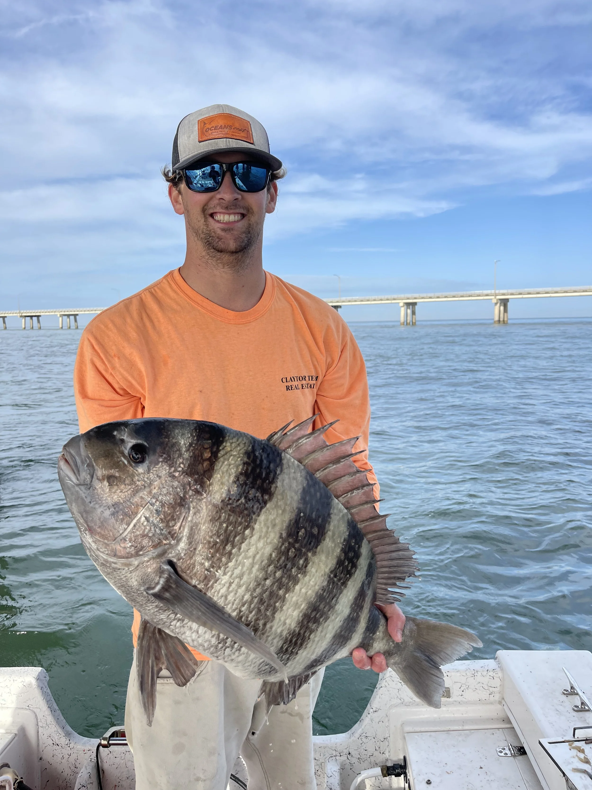 Man on boat holding a large fish with a bridge in the background.