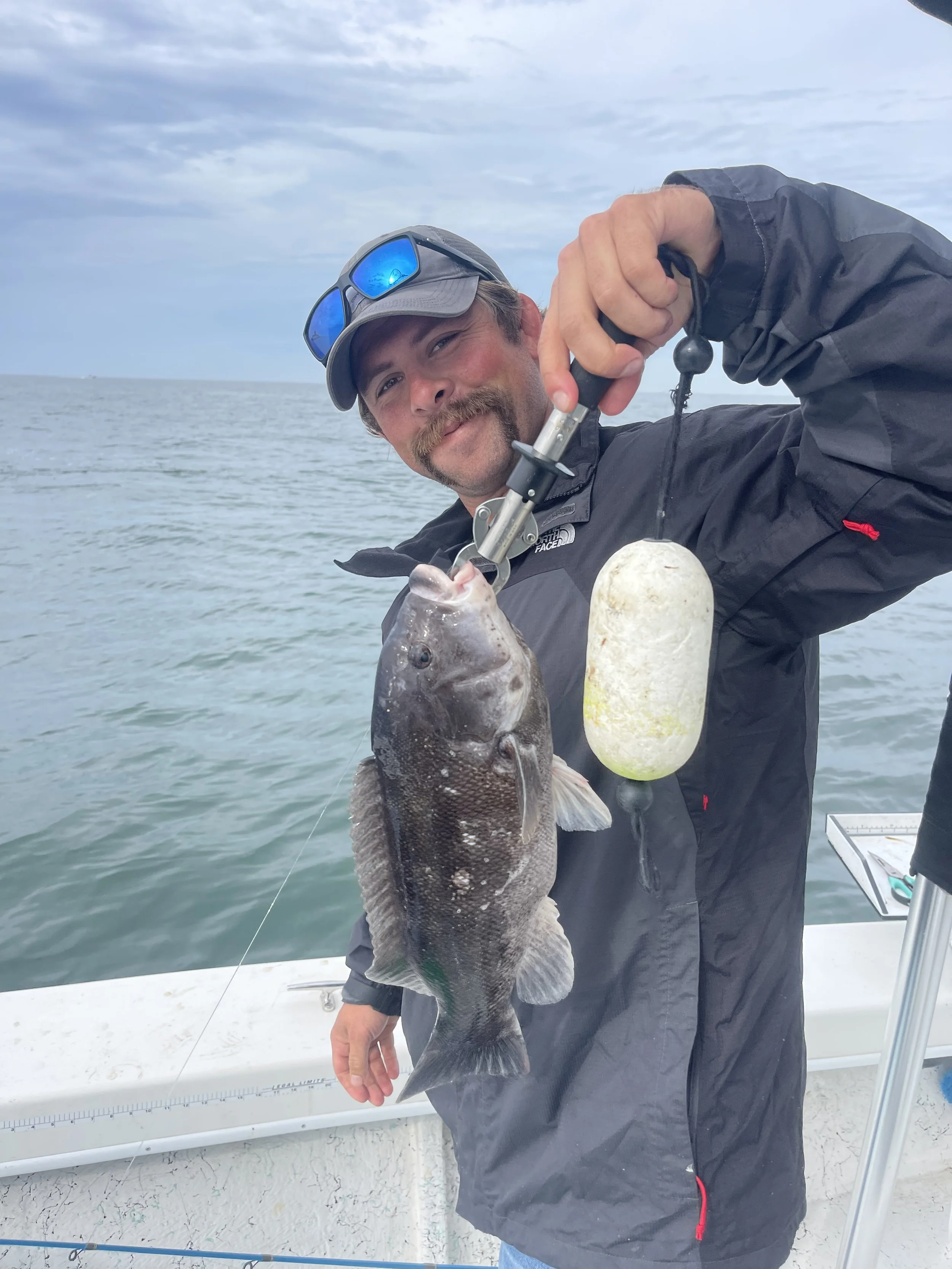 A man holding a fishing rod, displaying a caught fish on a boat with water and cloudy sky in the background.