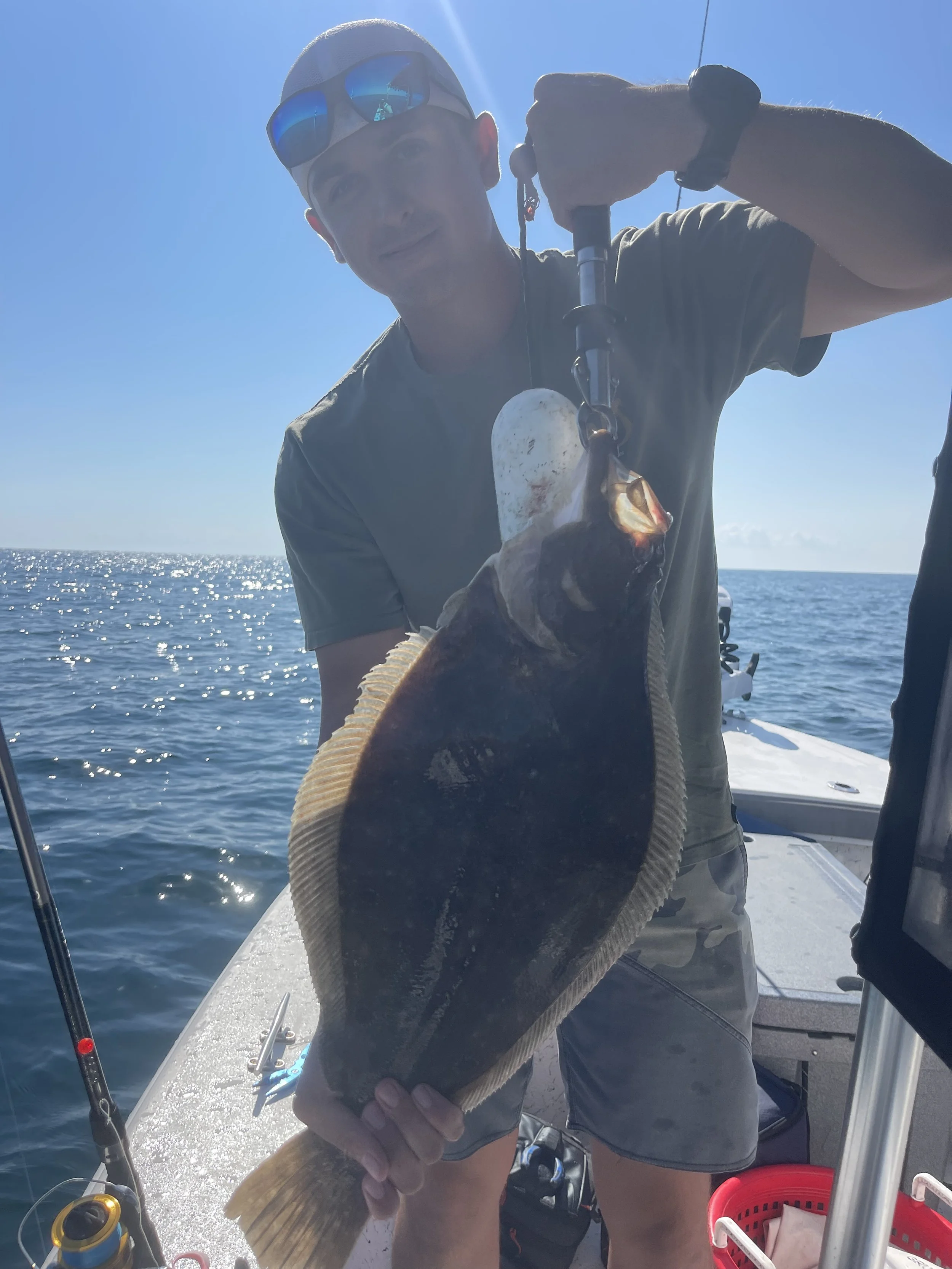 A man on a boat holding a large fish he caught, with the ocean and blue sky in the background.
