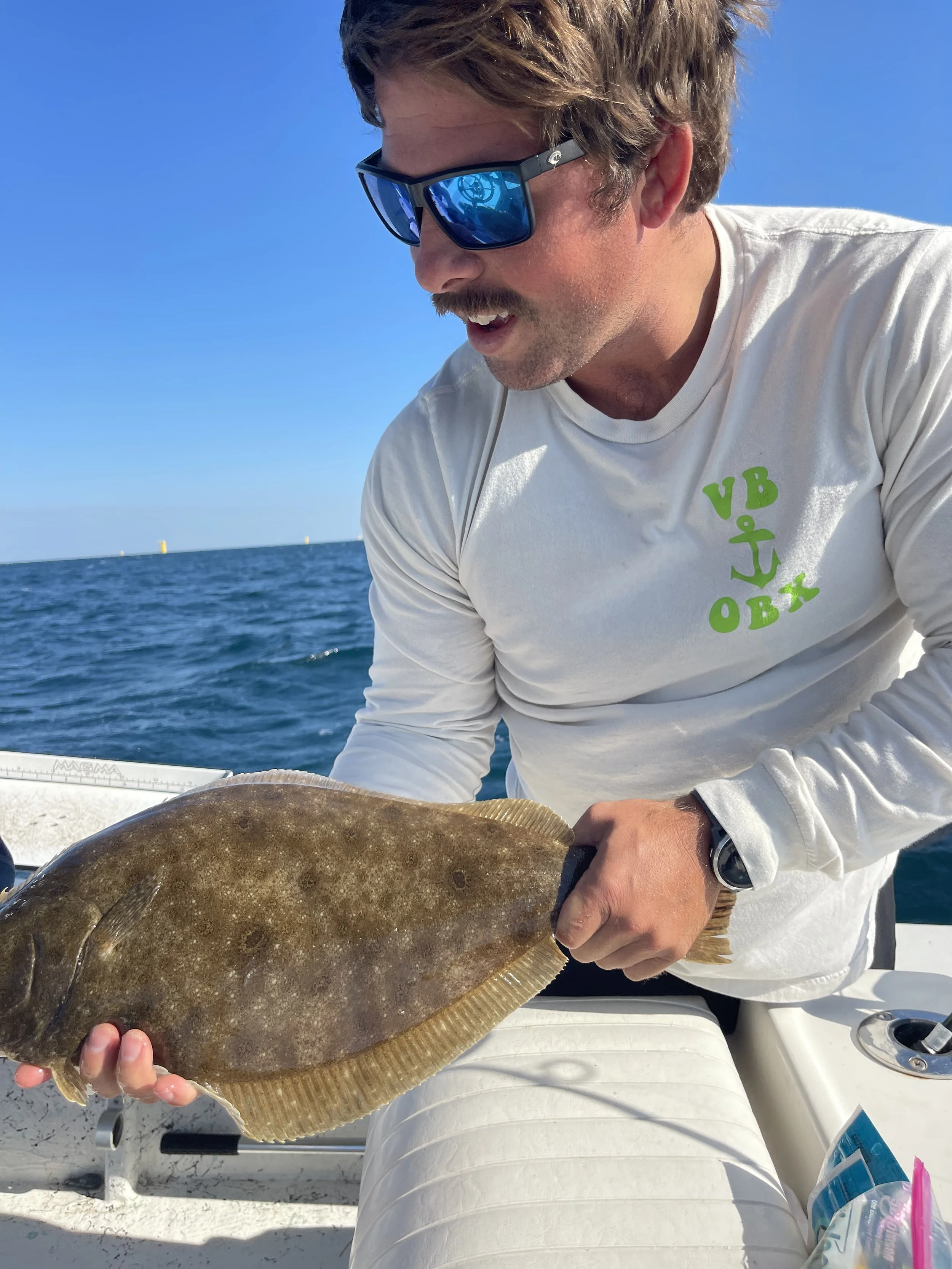 Man with sunglasses holding a flatfish on a boat in the ocean.