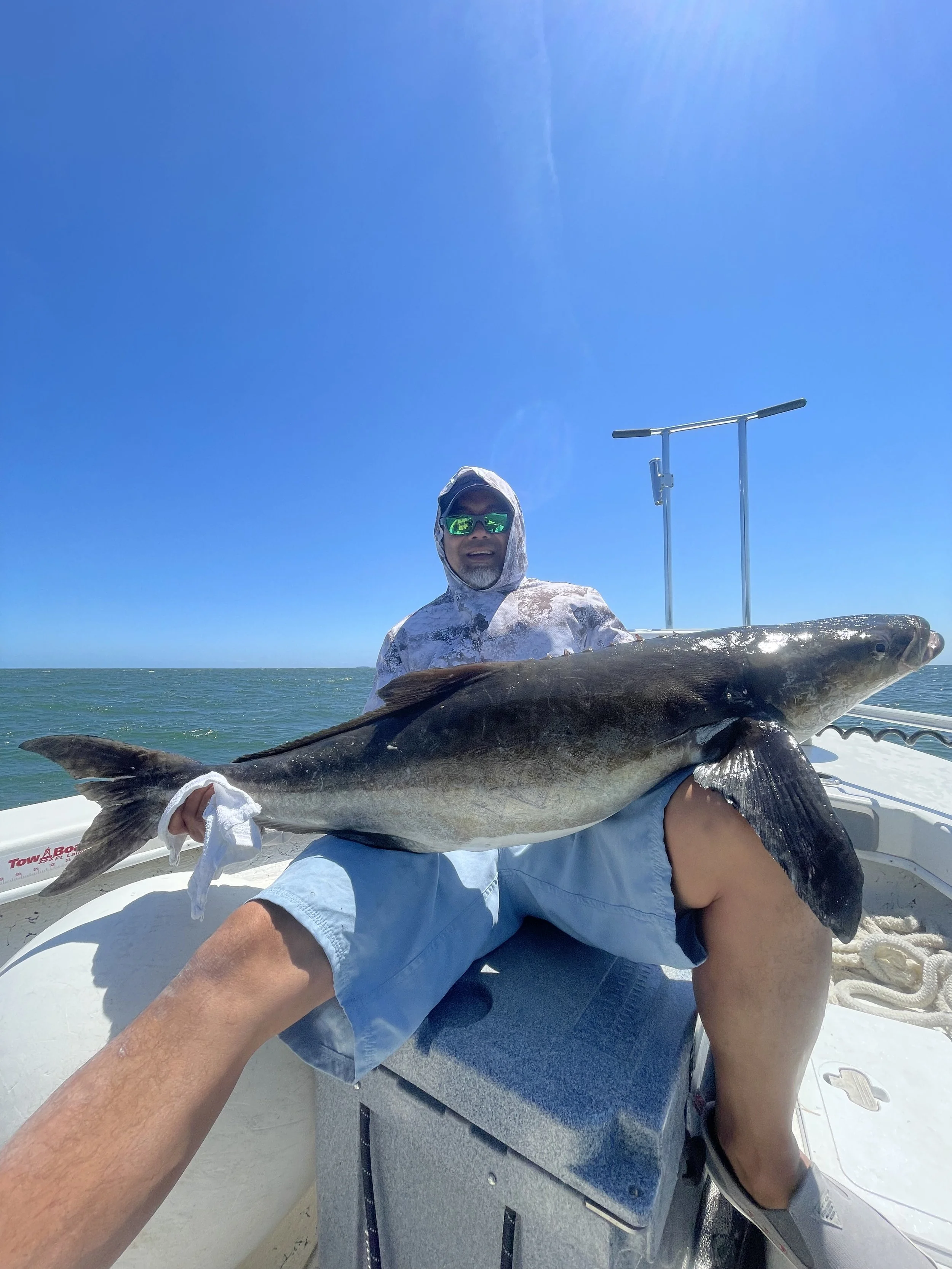 Man holding a large fish on a boat in the ocean under a clear blue sky.