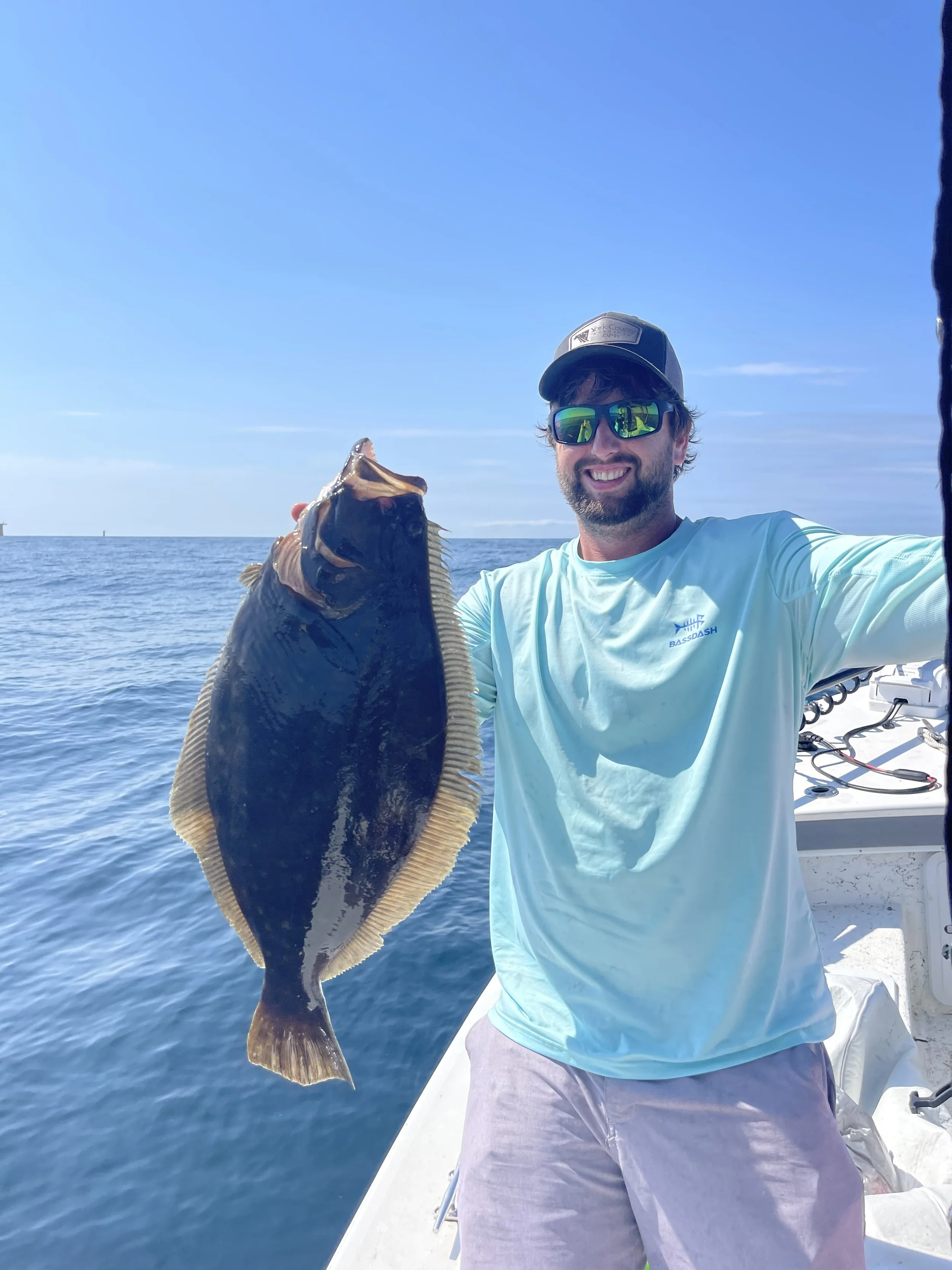 Man holding a large fish on a boat in the ocean on a sunny day, smiling at the camera.