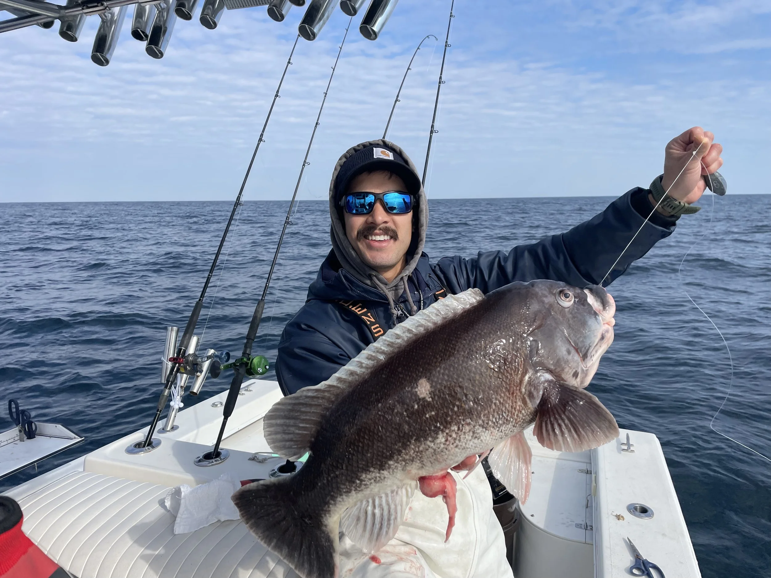 Man on a boat holding a large fish he caught while fishing in the ocean.
