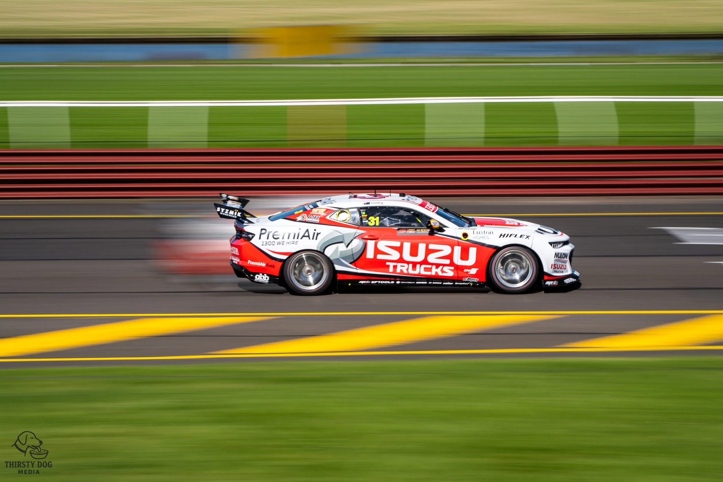Race car with Isuzu Trucks livery speeding on a racetrack, with blurred background indicating high speed.