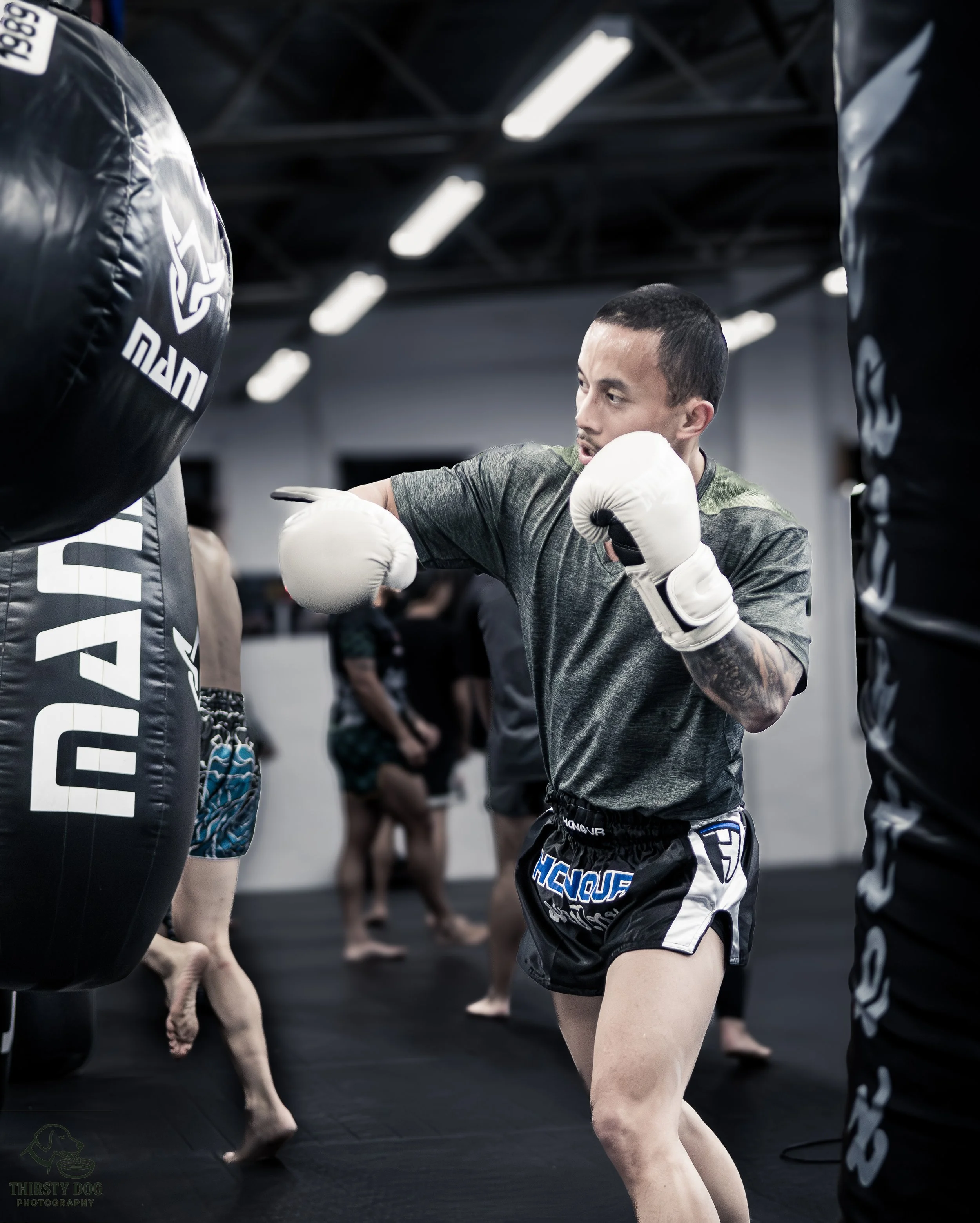 A man practicing boxing in a gym, wearing gloves and shorts, sparring with a punching bag.