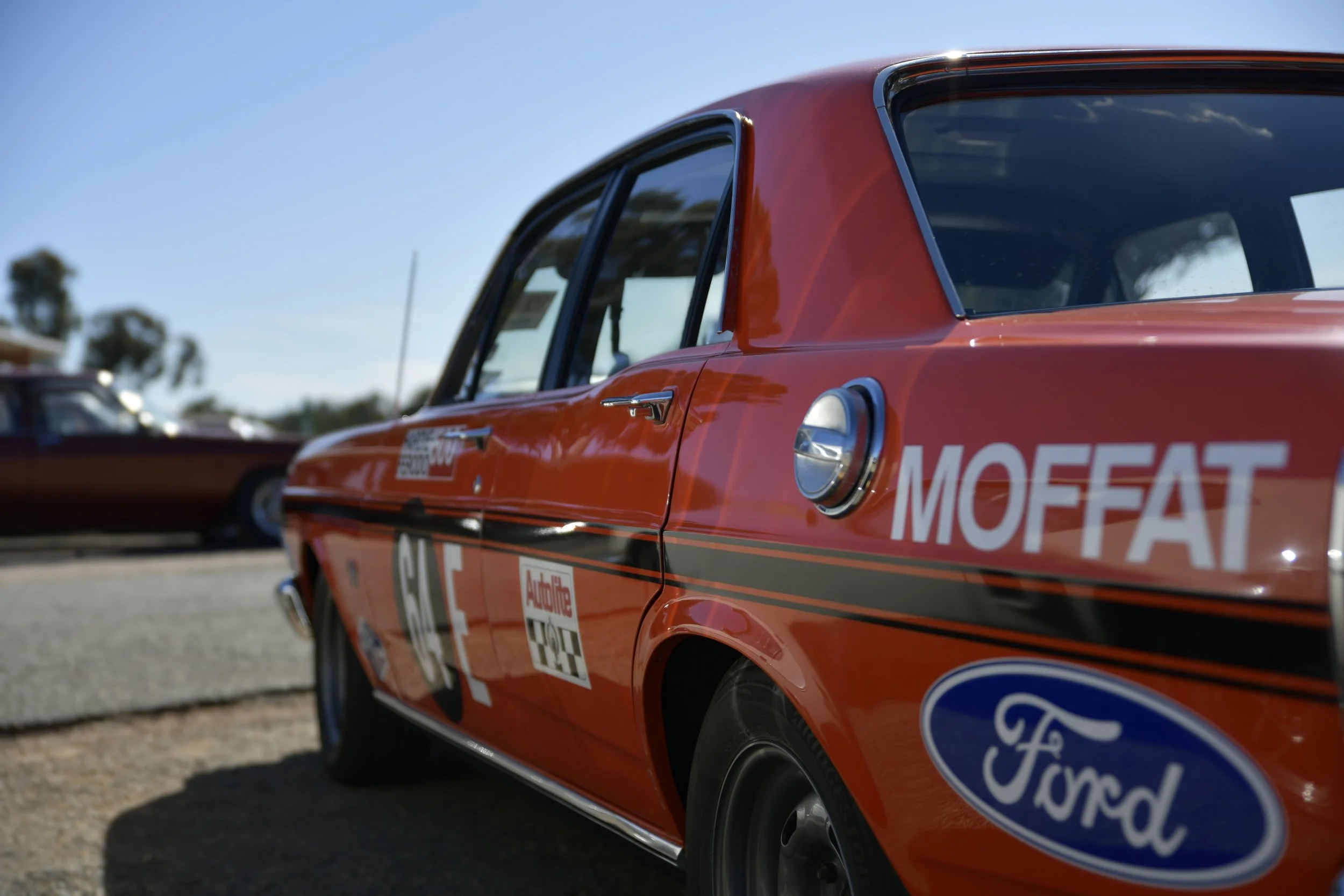 Red vintage race car with Ford logo and MOFFAT decals parked outdoors on a sunny day.