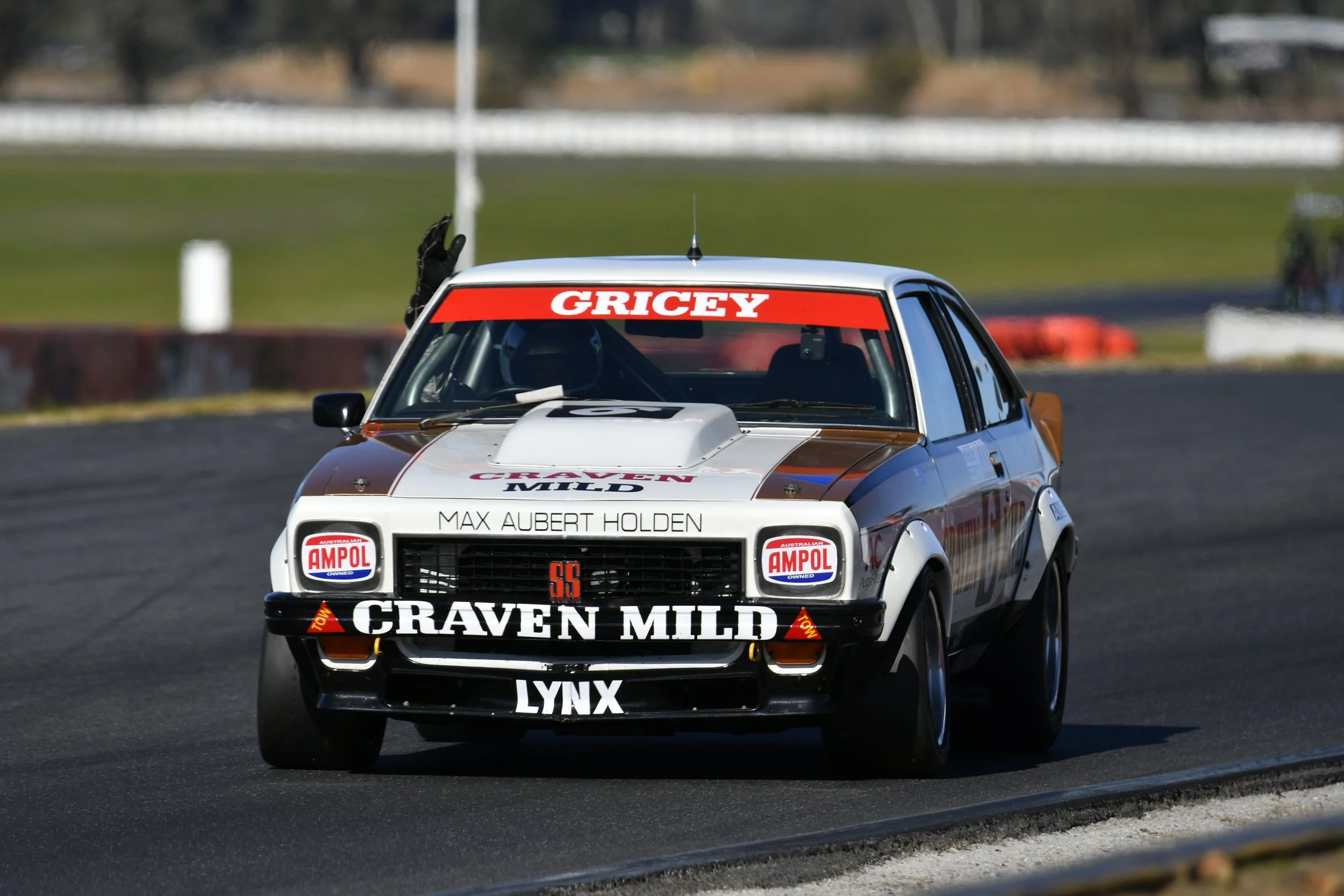 A race car on a track with various sponsor decals, including "Craven Mild," "Ampol," and "Lynx," driven by Max Aubert Holden.
