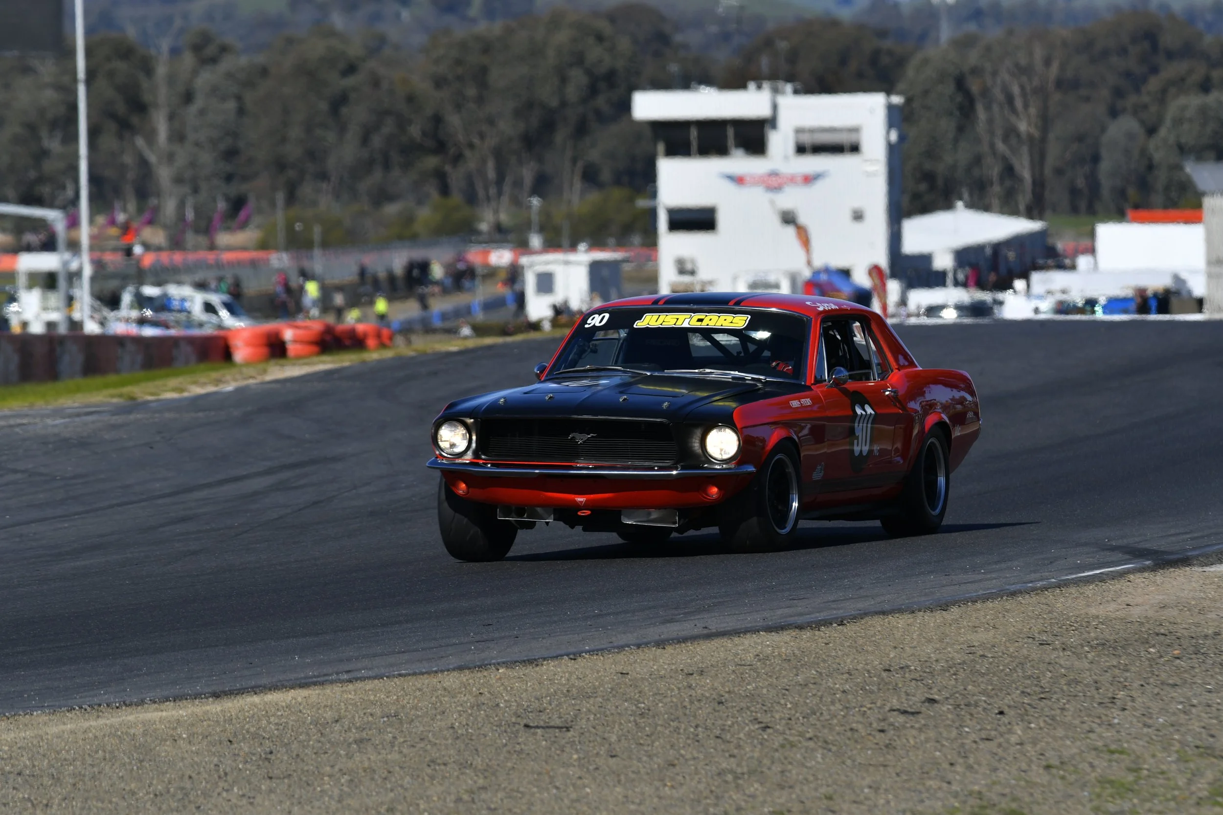A classic red and black vintage race car on a racetrack during a daytime race.