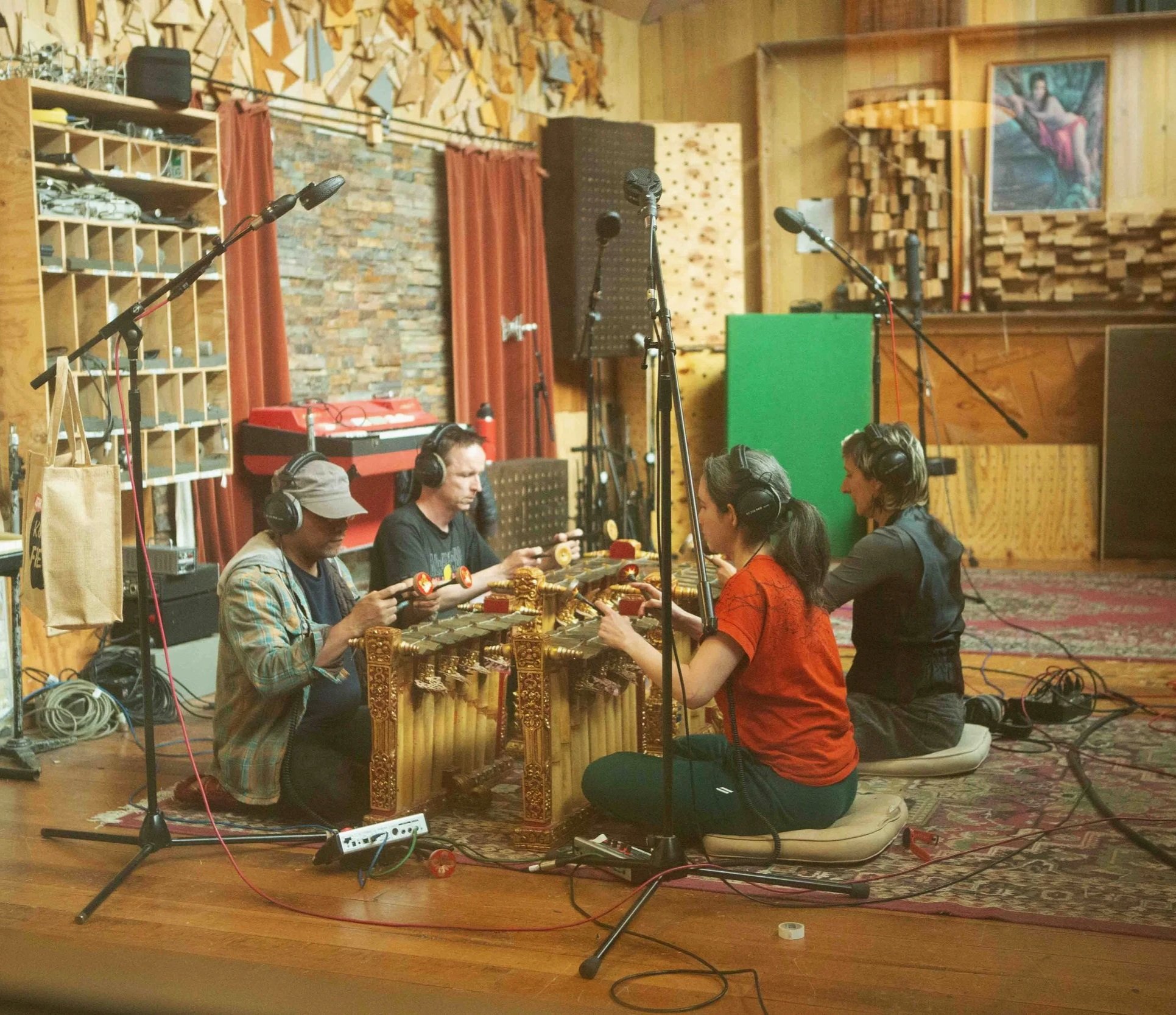 Four people sitting on cushions in a recording studio playing traditional wooden musical instruments, with microphones set up around them.