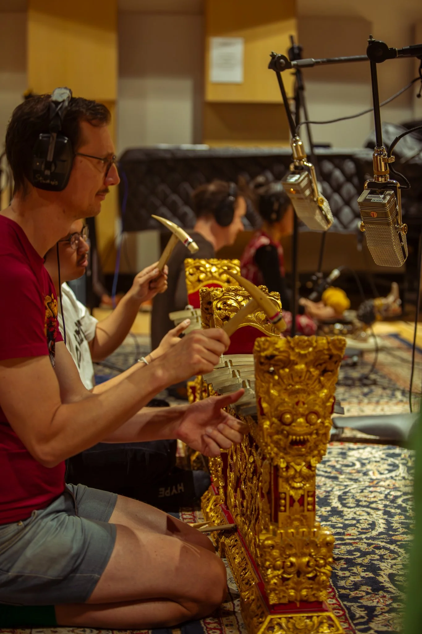 People participating in a traditional cultural performance, playing gold gilded musical instruments resembling dragons, in a room with microphones and a patterned rug.