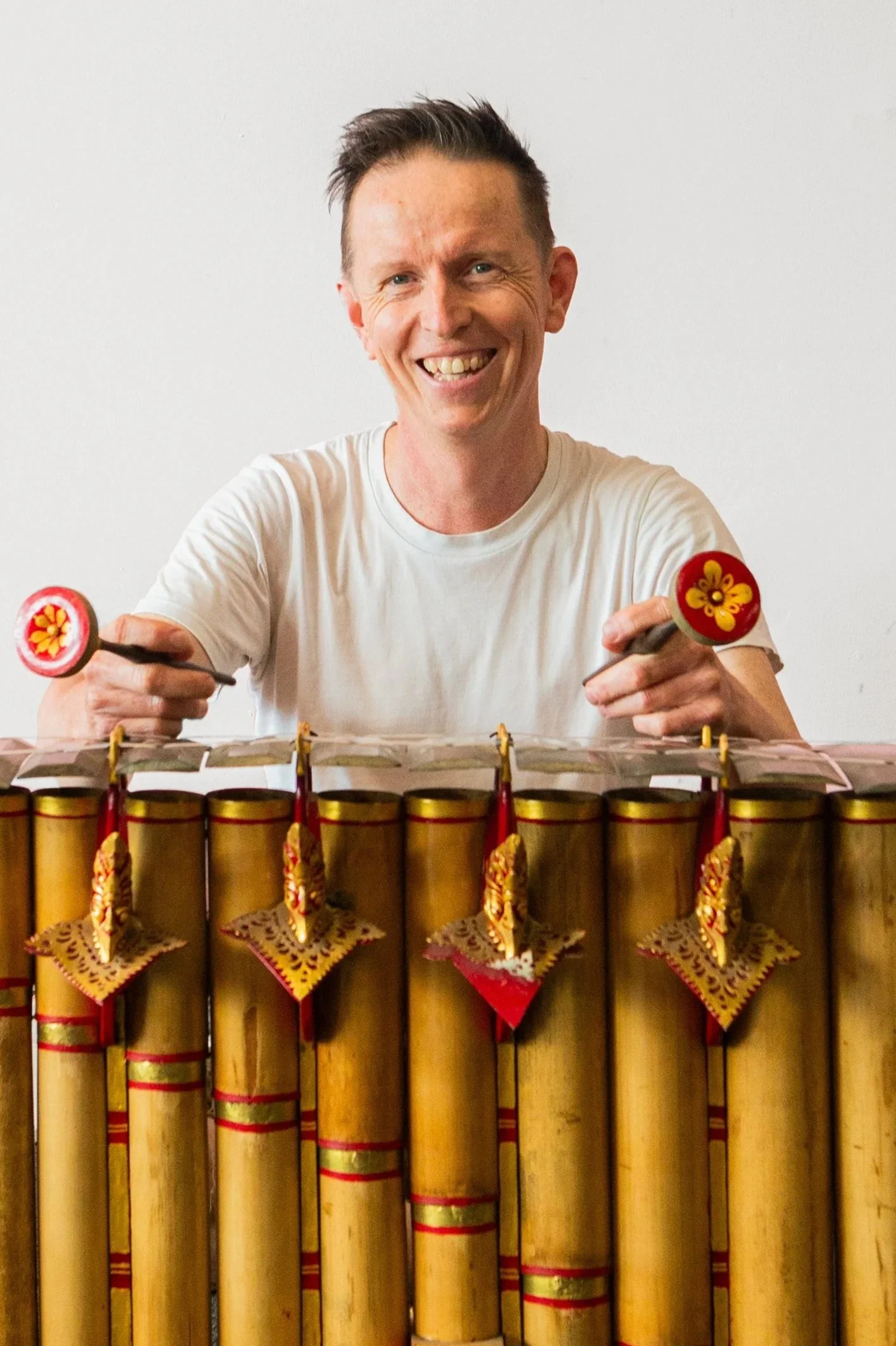 A man smiling and holding two paddles, sitting behind a display of fireworks.