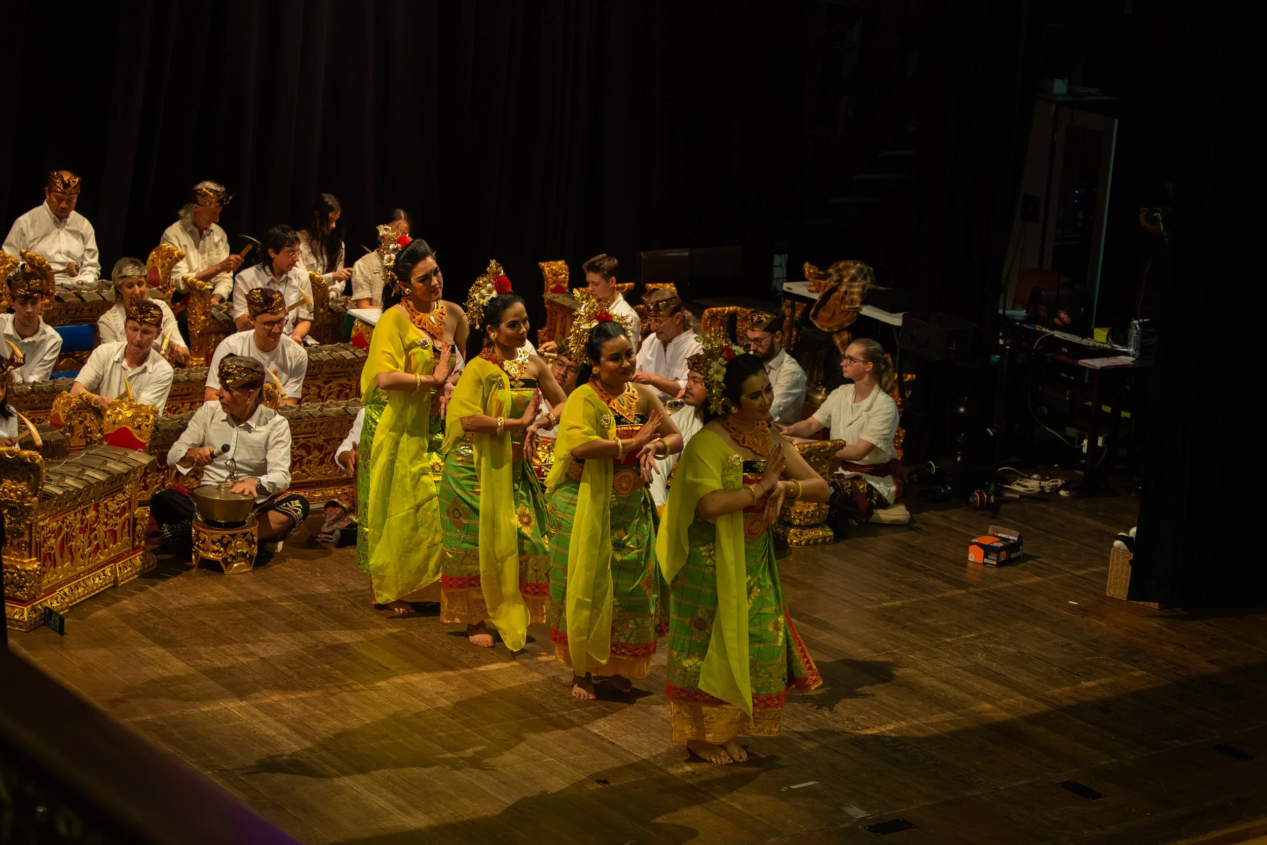 Performers in traditional Indonesian attire dancing on stage with musicians playing instruments in the background.