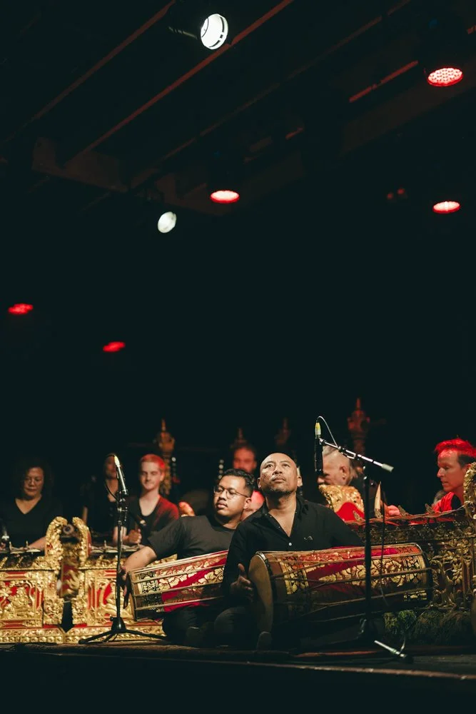 Group of musicians with traditional Asian instruments performing on stage, with colorful ornate decorations.