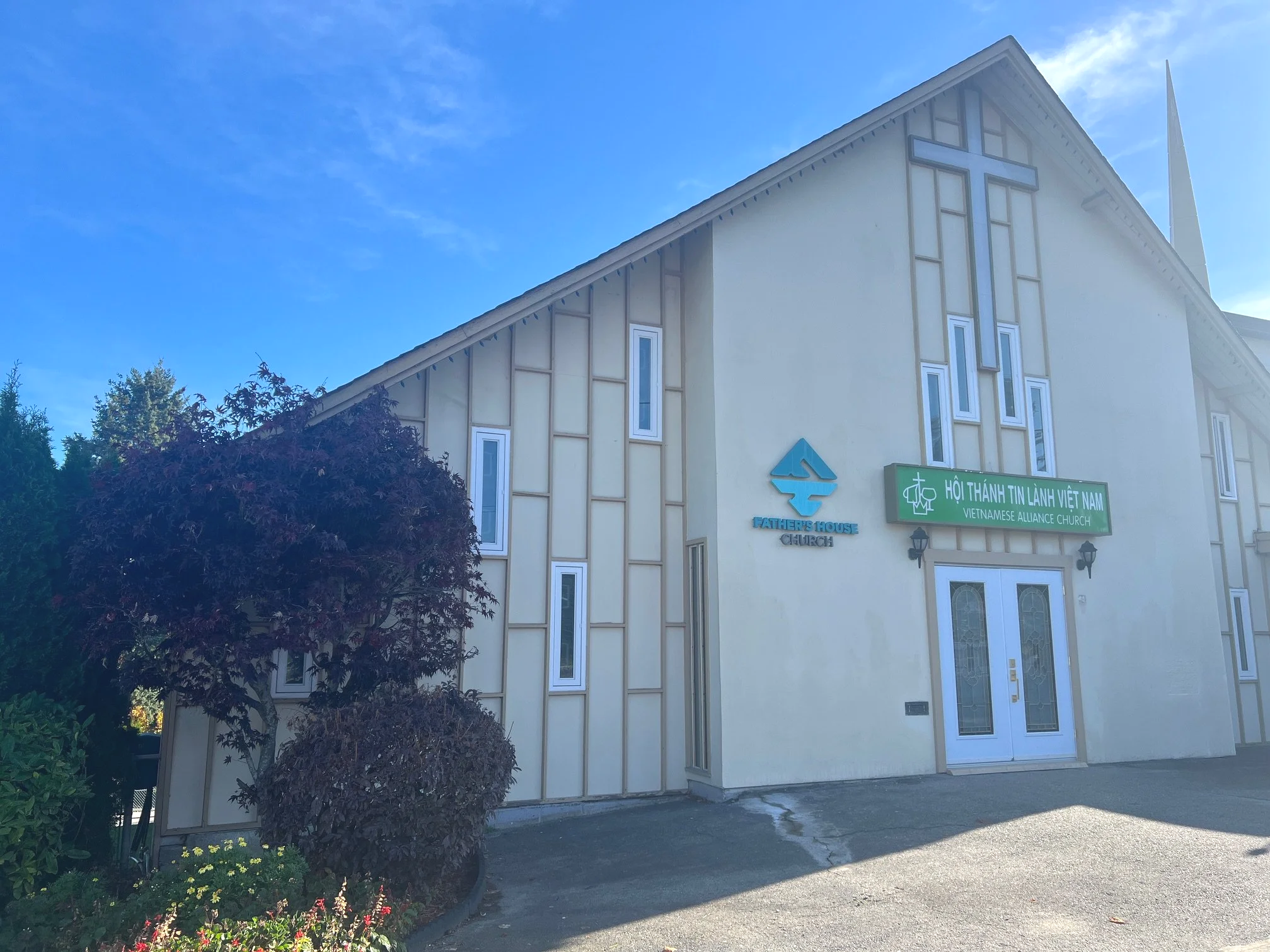 Front view of Vietnamese Alliance Church building with a cross, trees, and a blue sky.