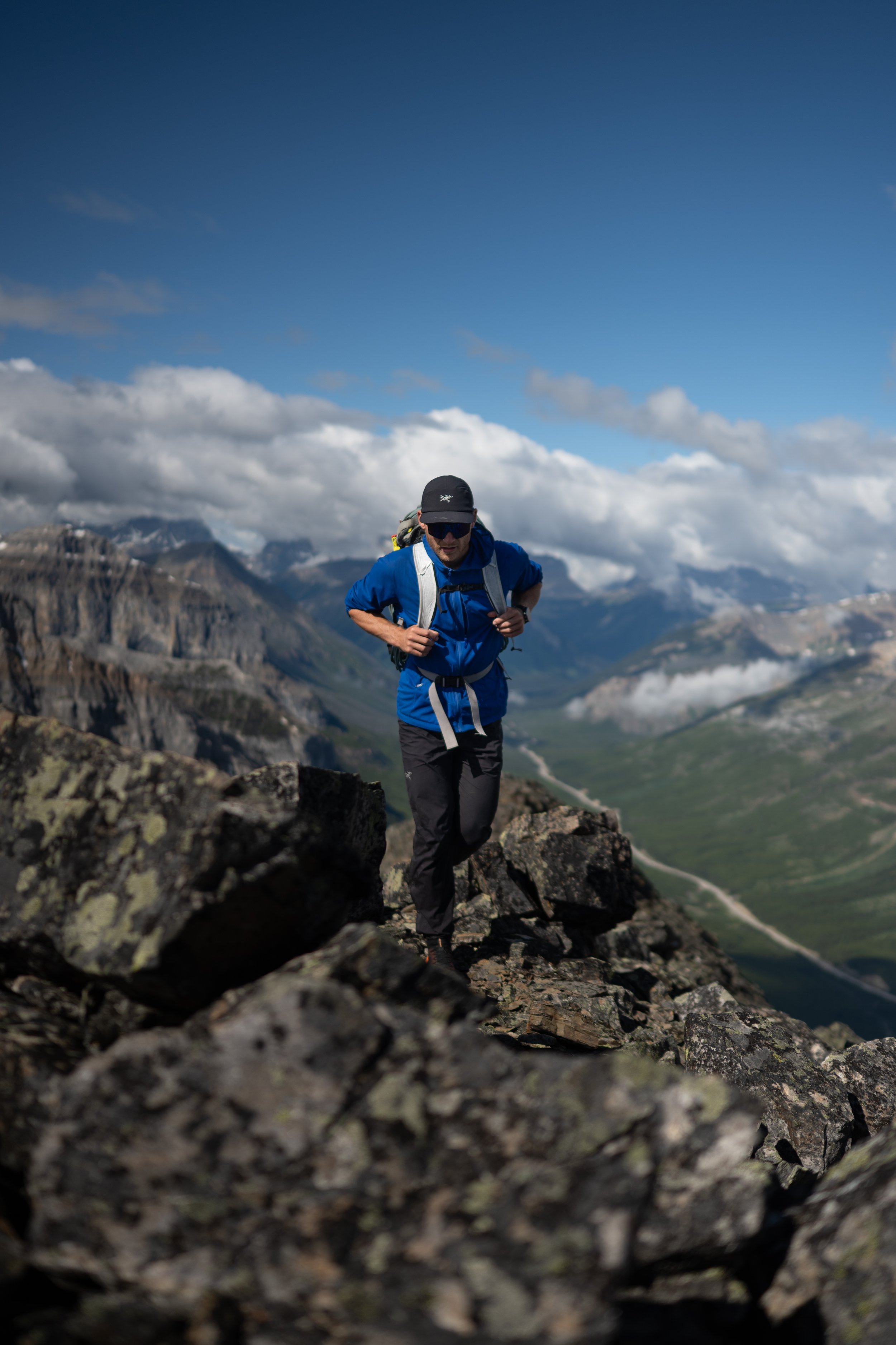 A person hiking on rocky terrain in a mountainous area with clouds and blue sky in the background.