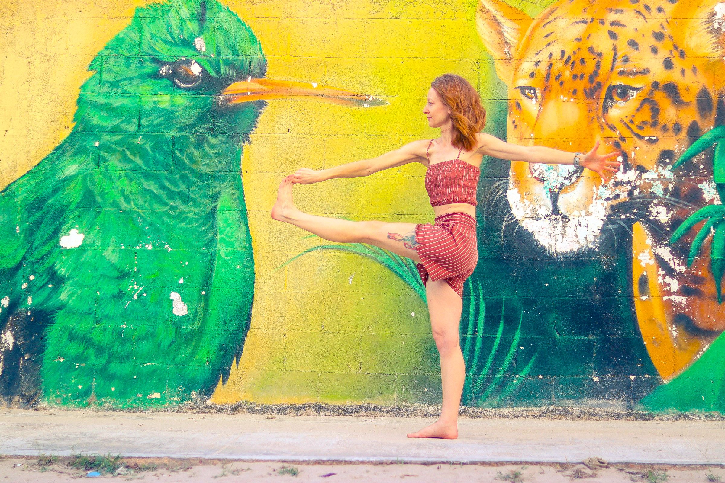 A woman practicing yoga in front of a colorful mural of a bird and a jaguar.