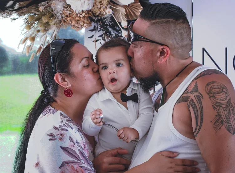 Natural wedding reception photography capturing a heartfelt family moment as two guests share a kiss with their baby during the celebration.