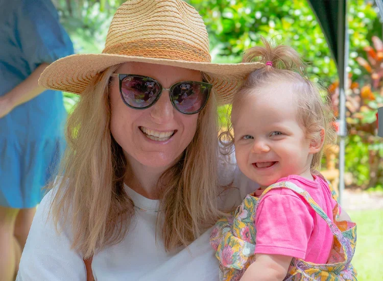 Natural family photography capturing a mother holding her baby daughter during a birthday celebration, photographed in a warm and candid documentary-style moment.