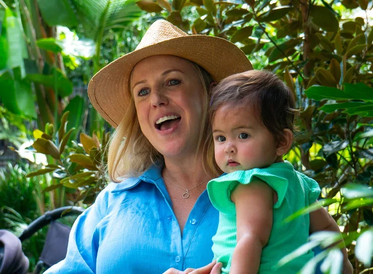 Natural family photography capturing a joyful mother smiling while holding her baby daughter during a birthday celebration, photographed in a warm and candid style.