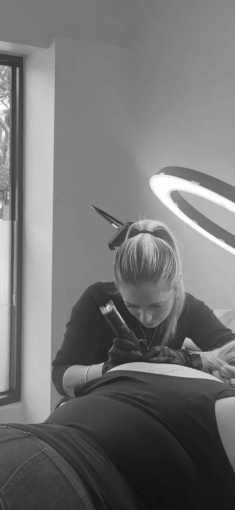 A tattoo artist working on a client's back in a studio with a bright overhead light.