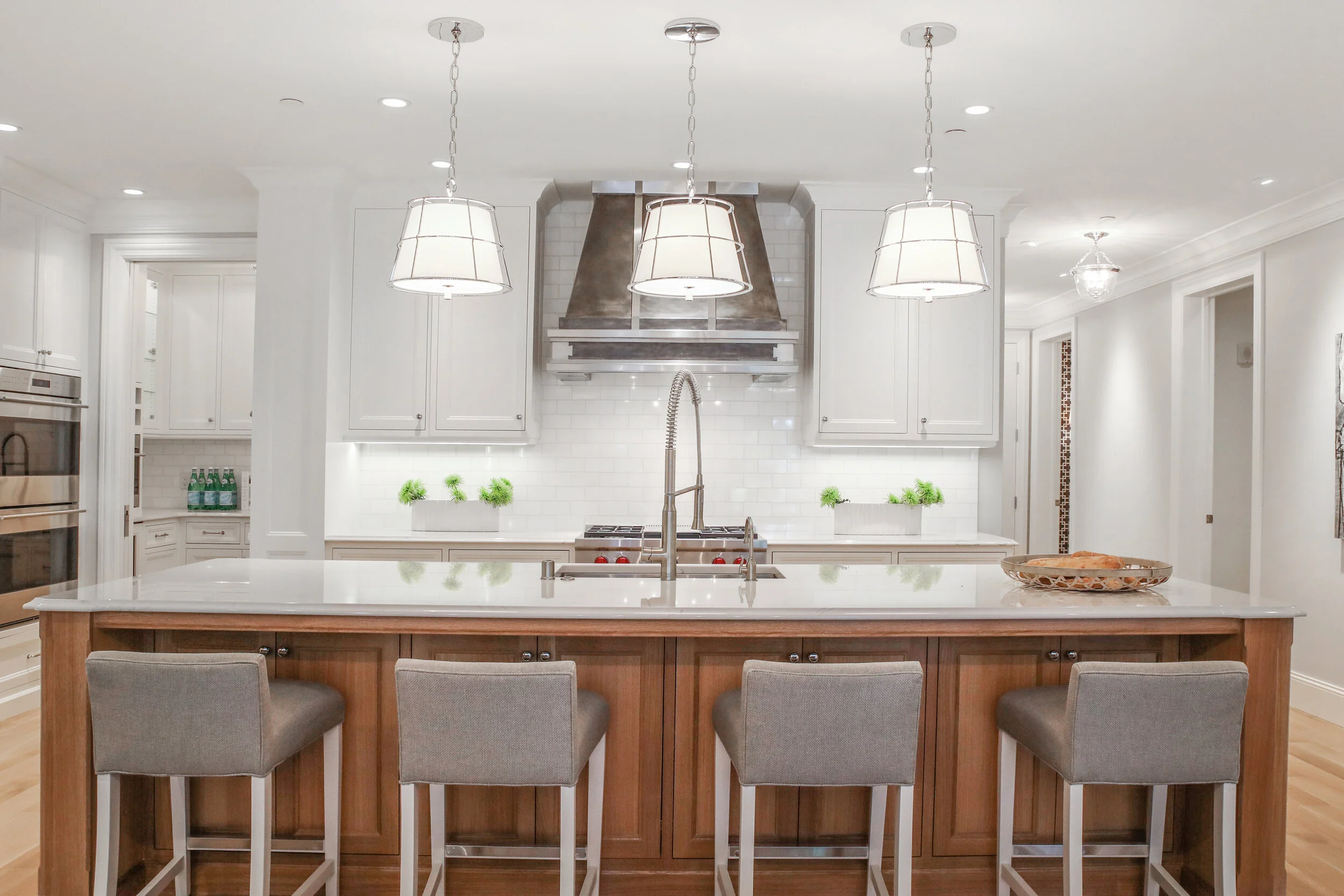 Modern kitchen with island, pendant lights, white cabinets, stainless steel appliances, and stools
