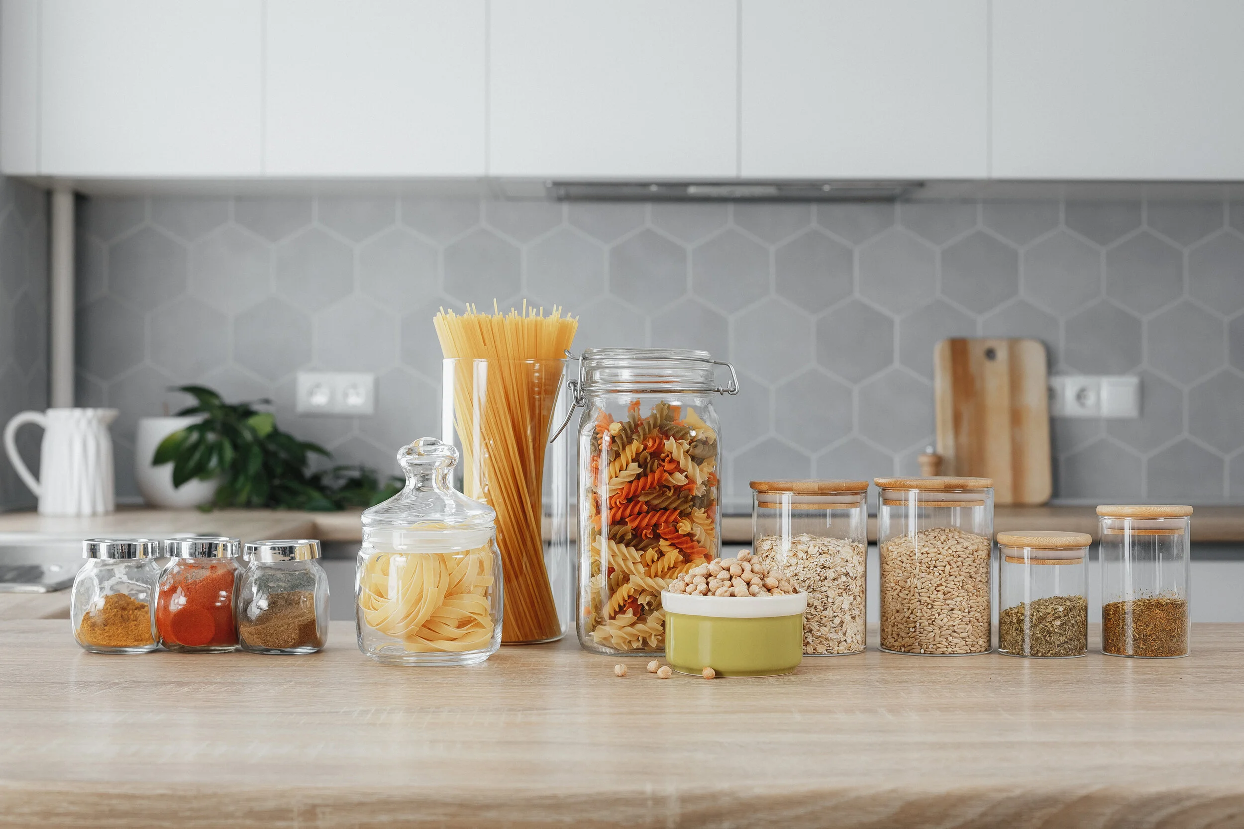 Kitchen counter with jars of pasta, spices, grains, and legumes in a modern kitchen setting.