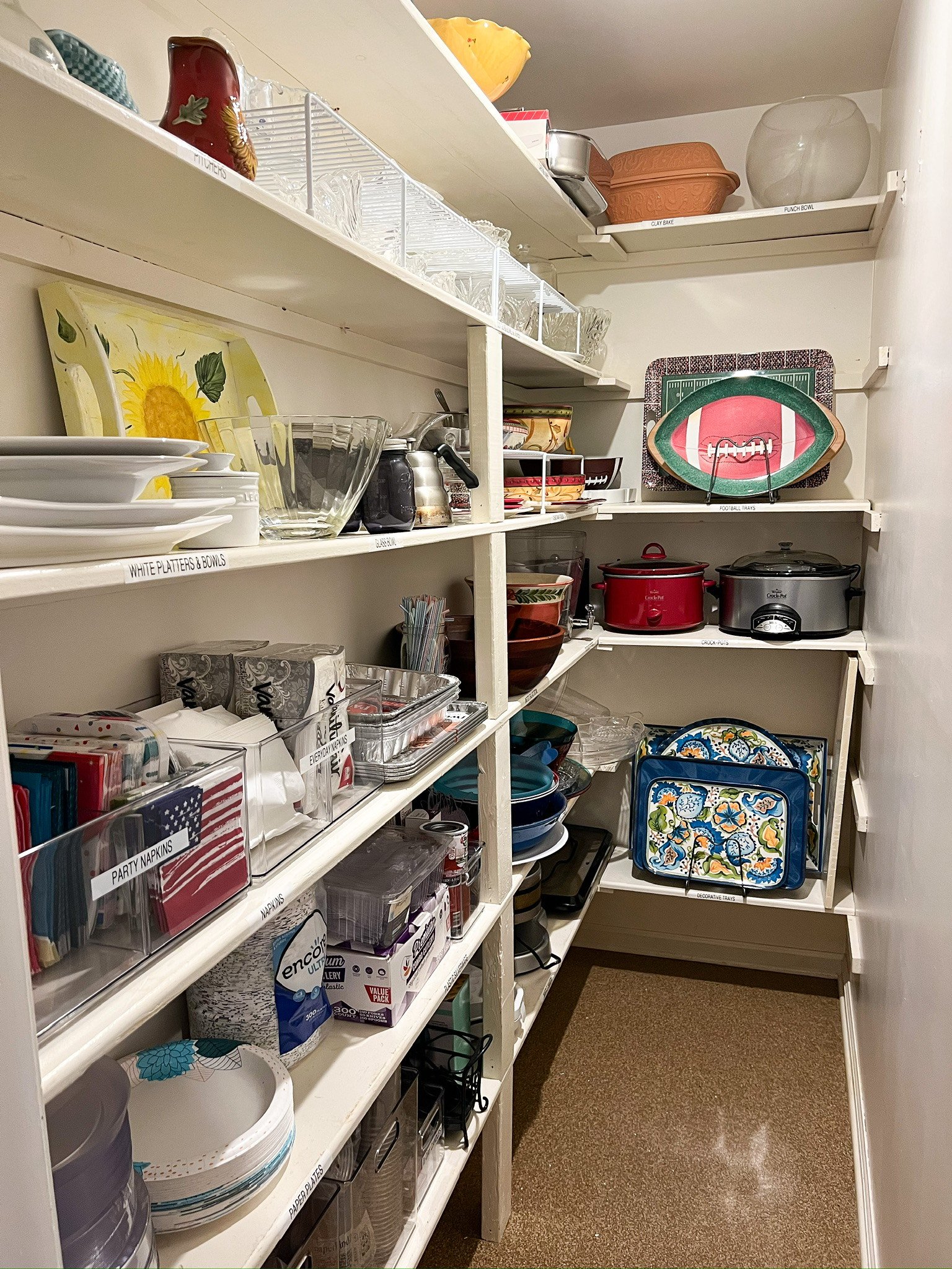 Organized pantry with shelves containing kitchen items like plates, bowls, serving dishes, slow cookers, napkins, and paper products. Professionally organized by Uncluttered Spaces located in Bucks County. 