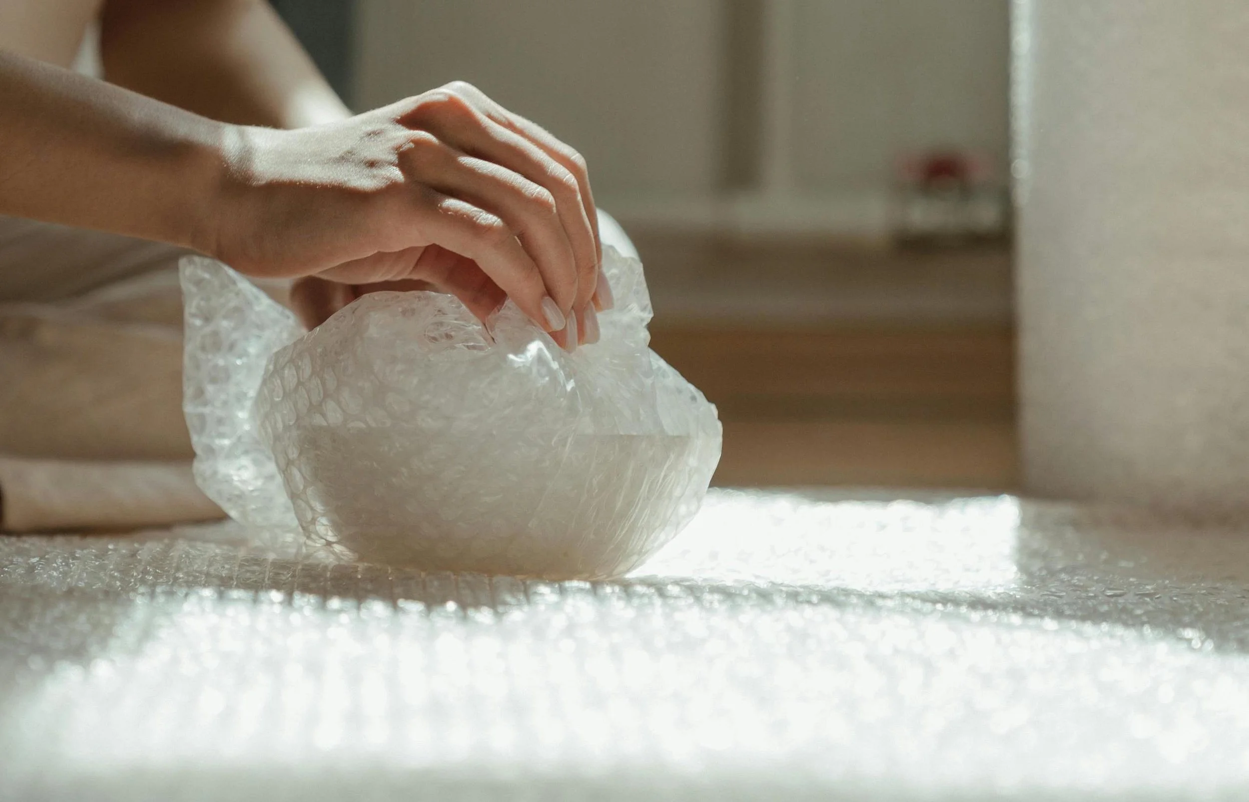 Hands carefully wrap a valuable item in bubble wrap