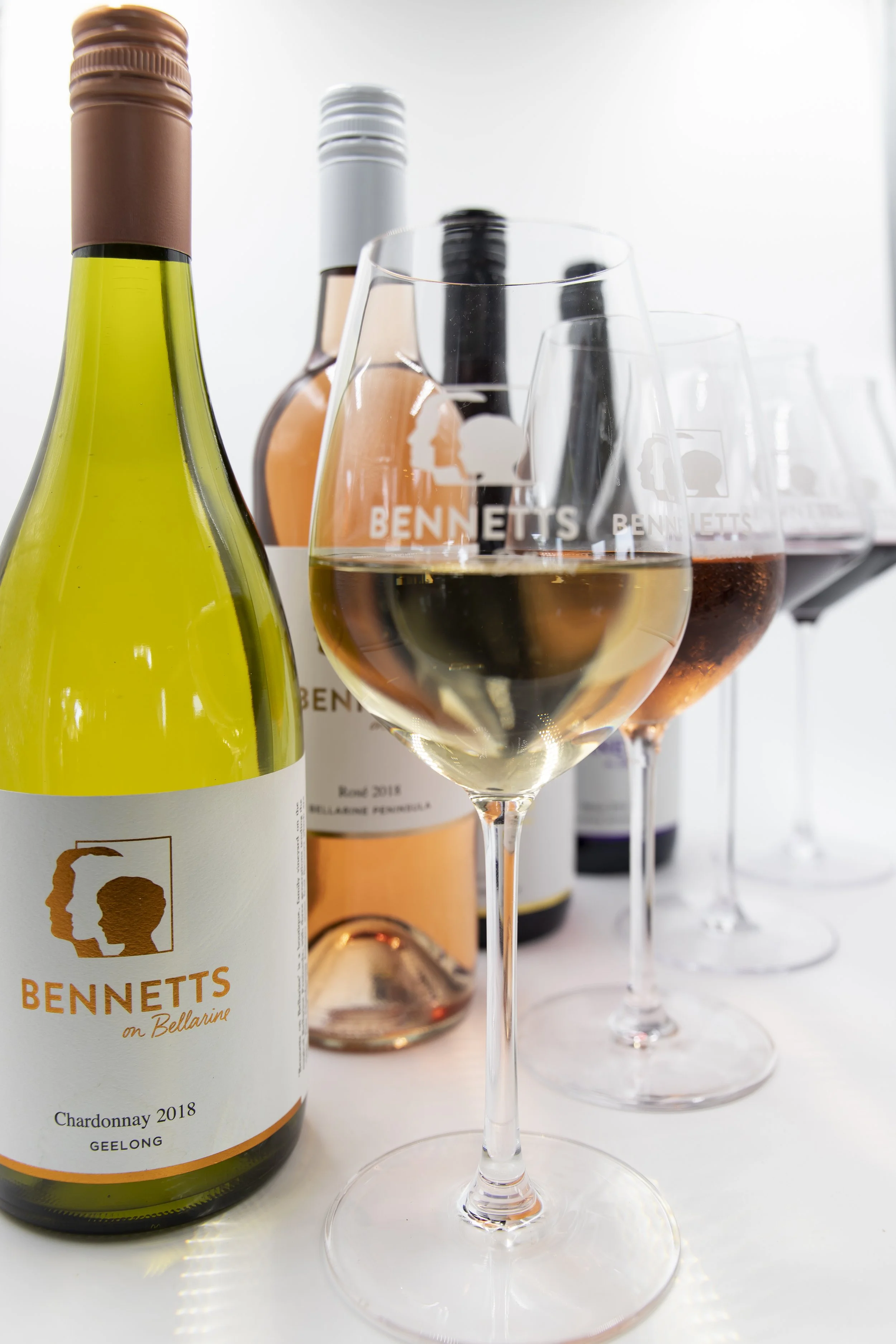 Several bottles of Bennetts wine and glasses of white and rose wine on a table.