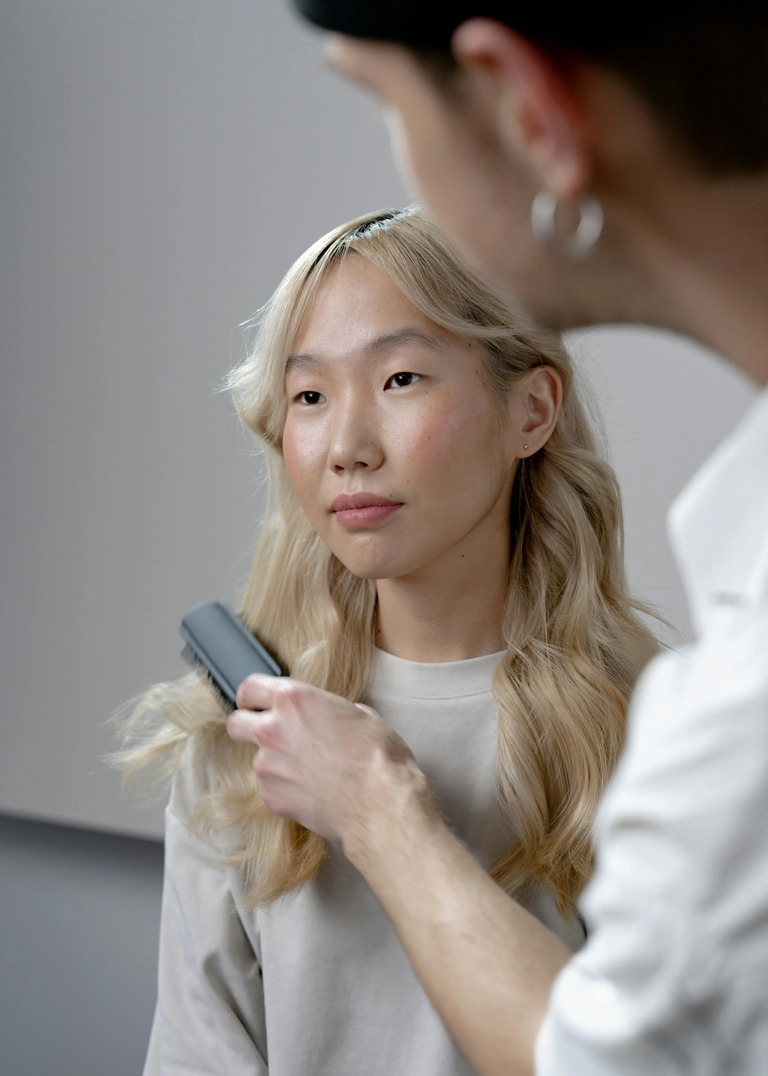 A woman with blonde hair getting her hair brushed by another person in a salon or similar setting.