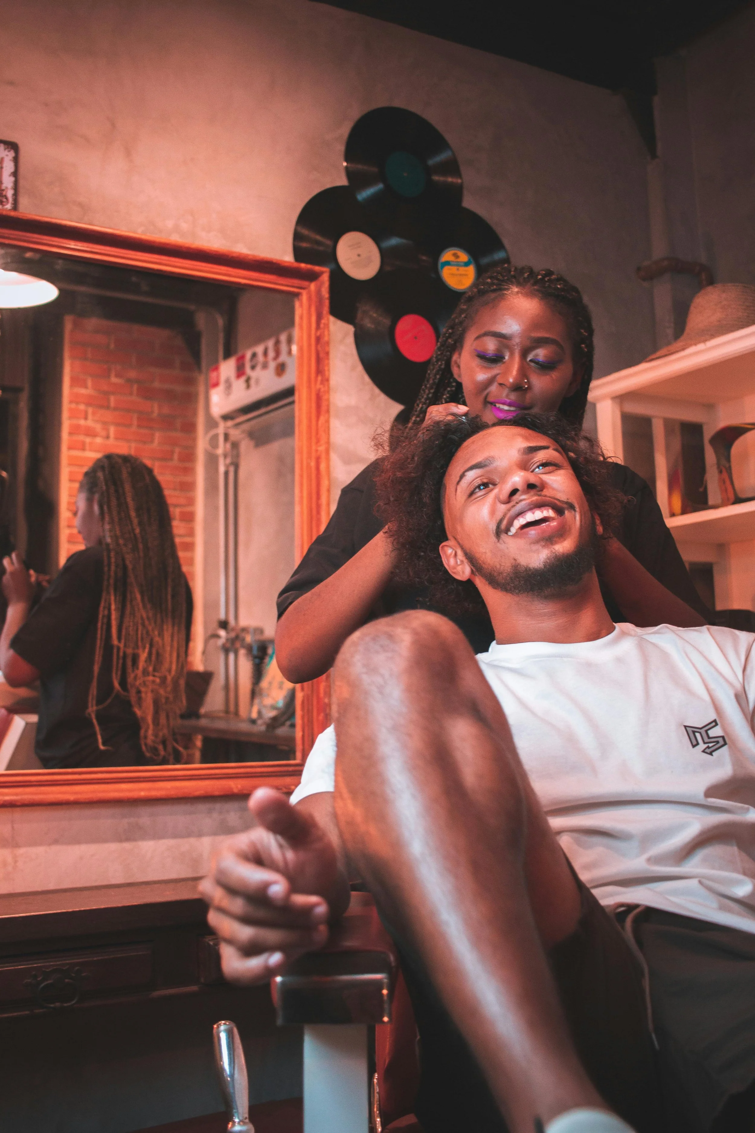 A woman and a man enjoying a moment together in a cozy room, with a woman behind the man in a playful gesture, surrounded by vinyl records on the wall.