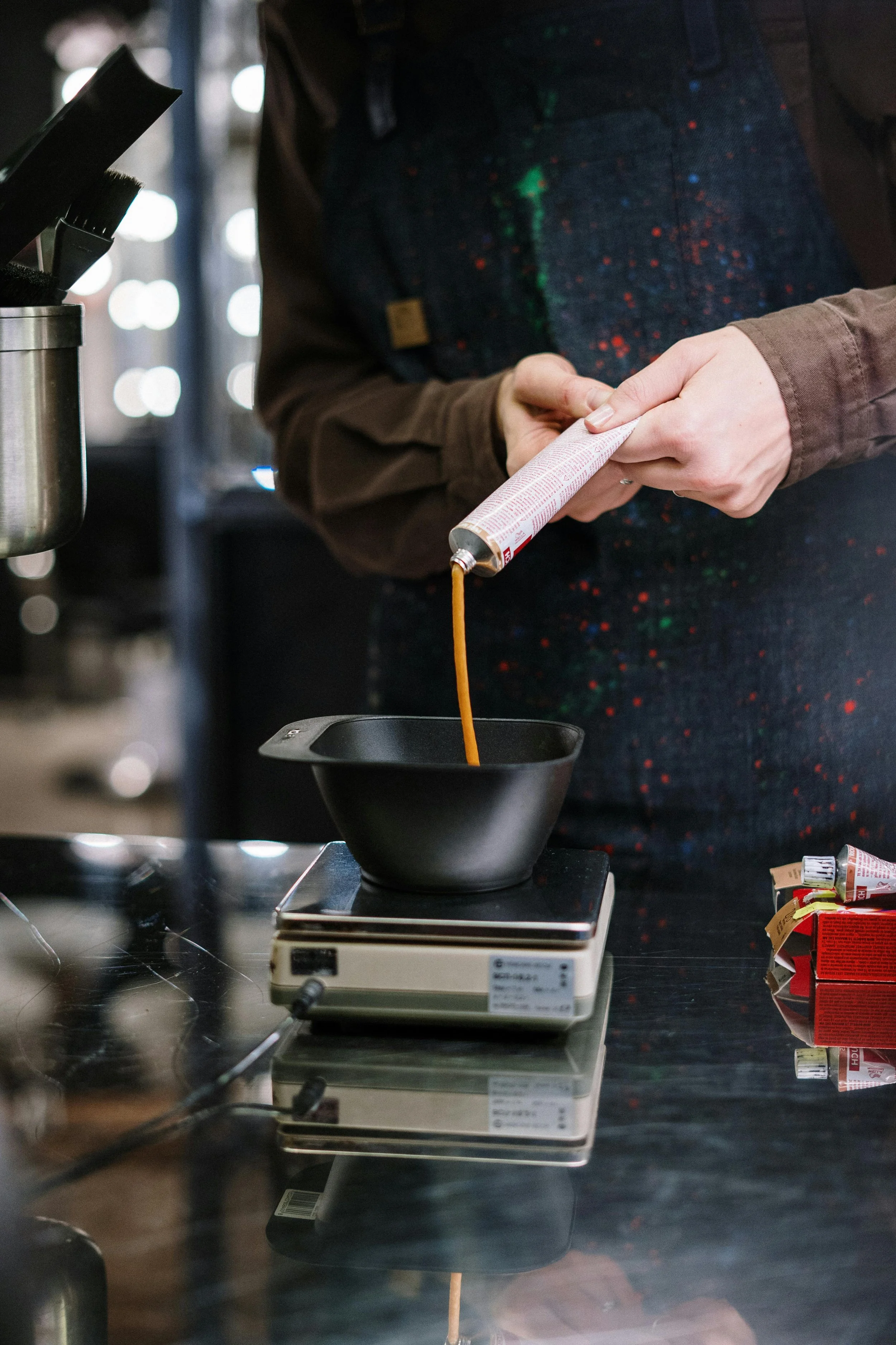 Person pouring coffee from a tube into a black bowl on a digital scale.