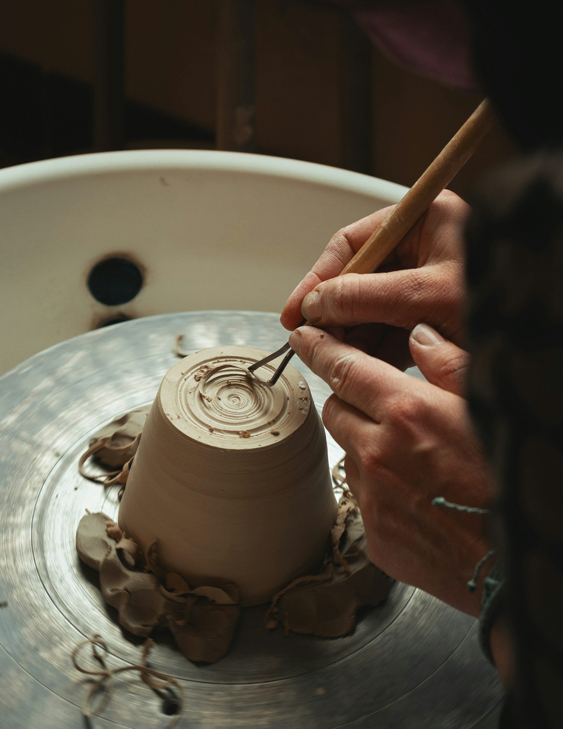 A person is shaping a ceramic piece on a pottery wheel, using their hands and tools to create detailed designs.