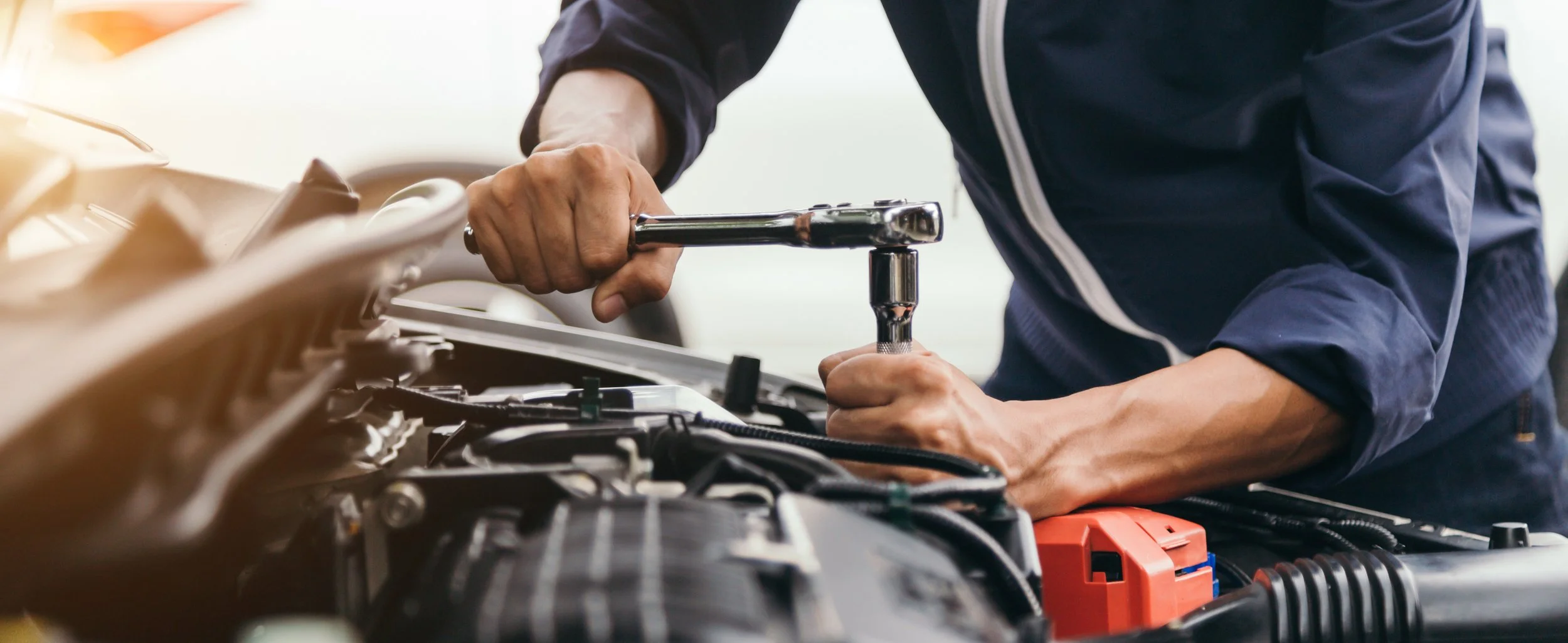 A mechanic using a wrench and a ratchet to repair a car engine in a garage.