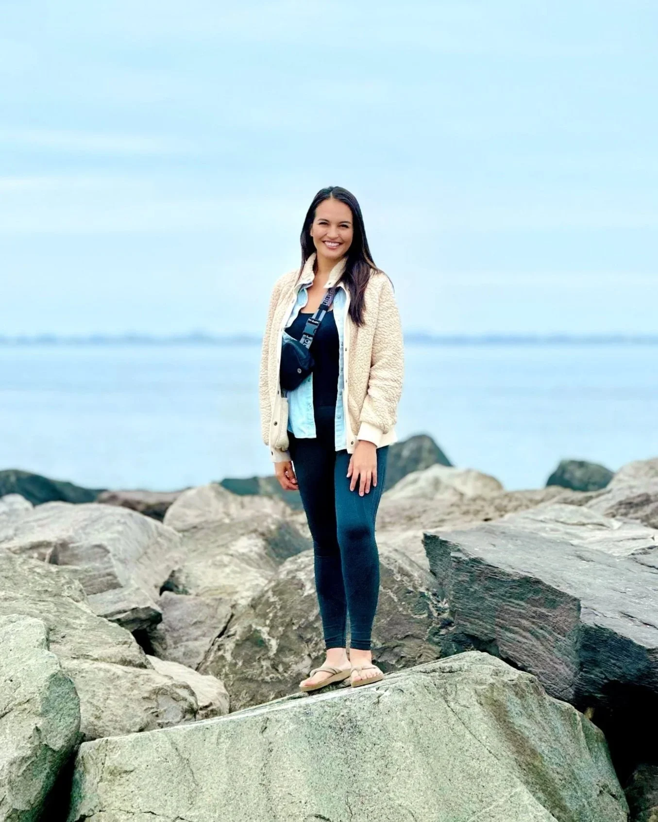 Rochelle Adriano standing on rocks near the water in coastal Washington state with a cloudy sky in the background.