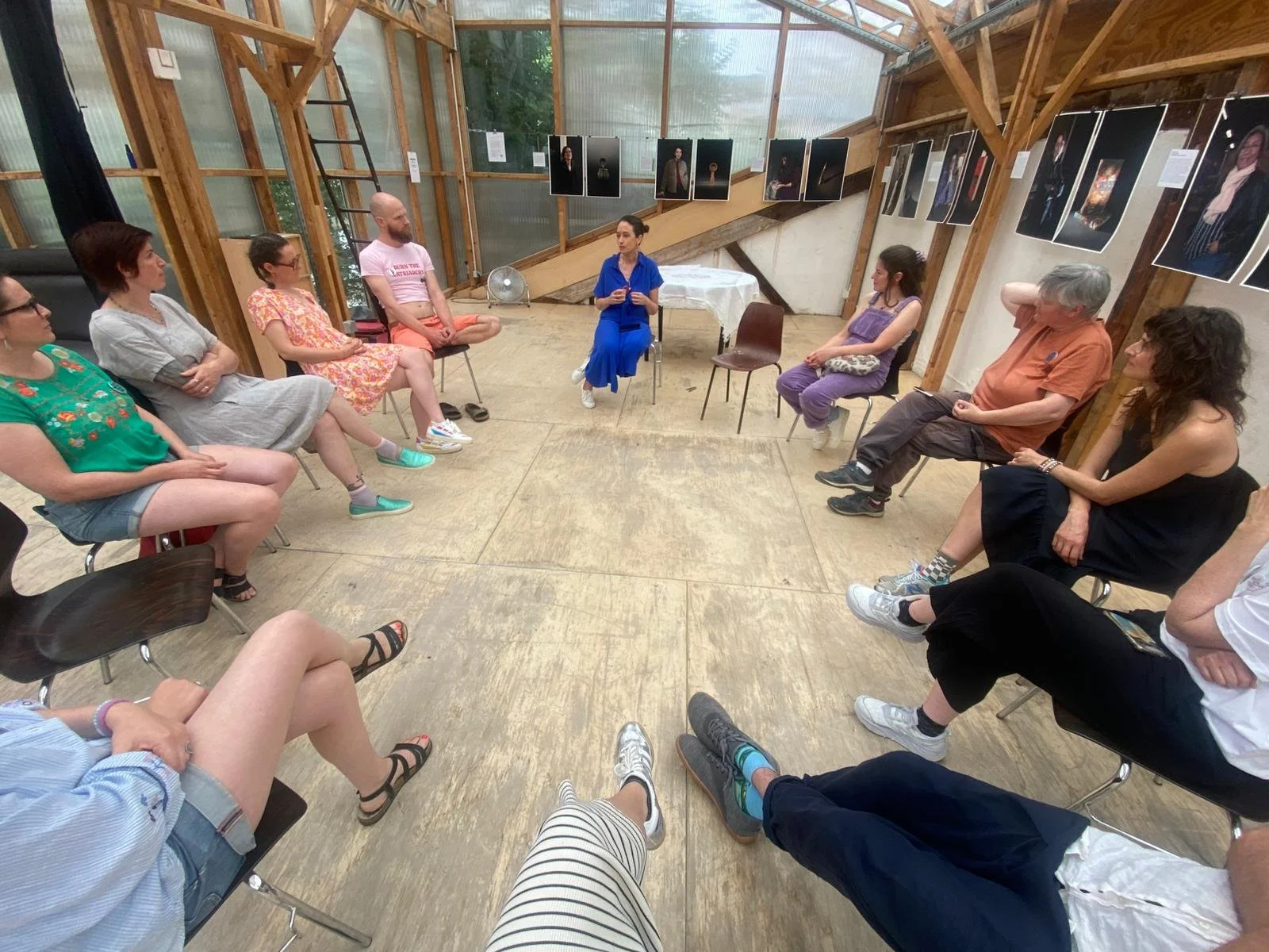 Groupe de personnes assises en cercle lors d'une discussion ou d'un atelier dans une salle en bois avec des photos affichées au mur.