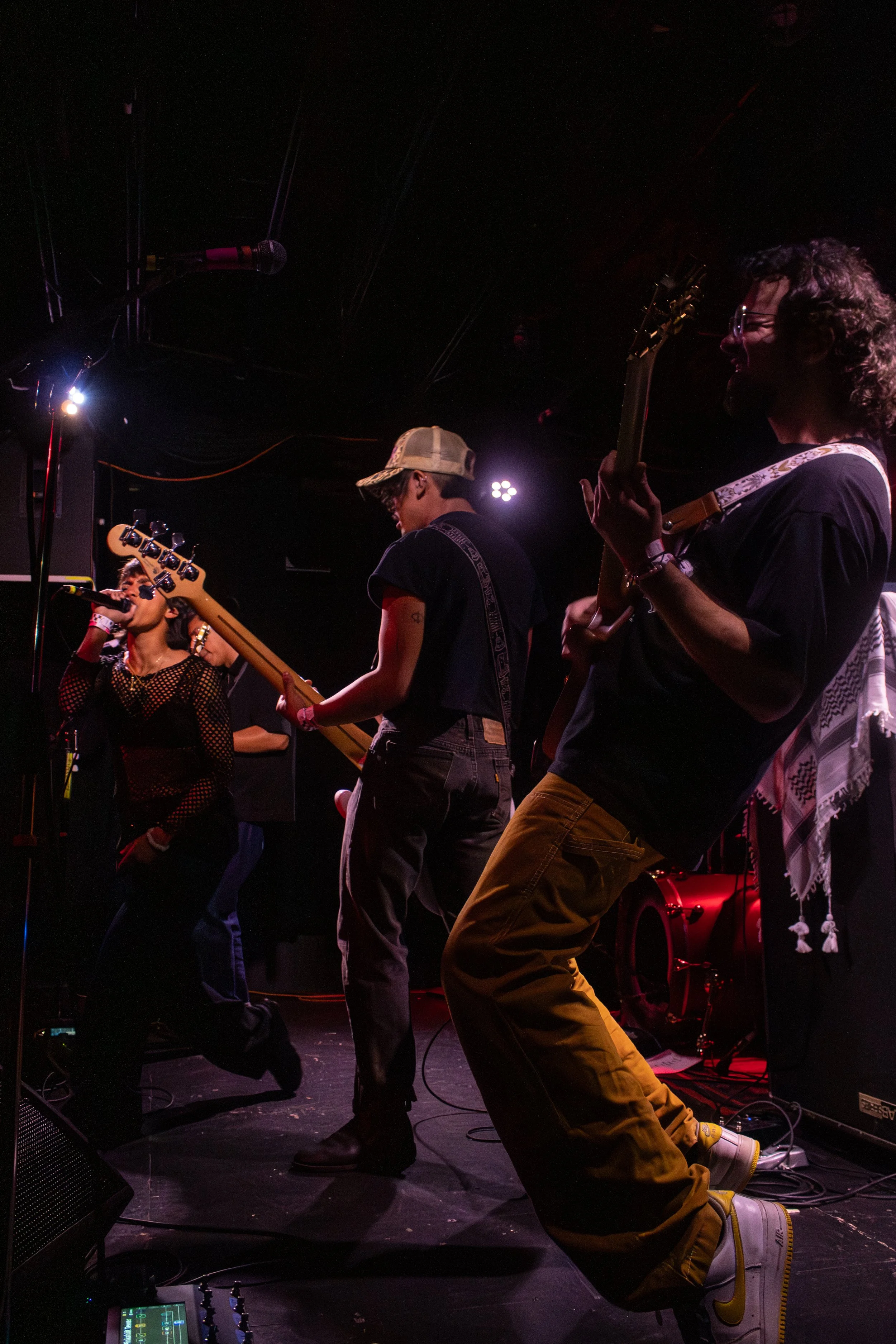 Performing band on stage, with vocals and guitars under dark stage lights.
