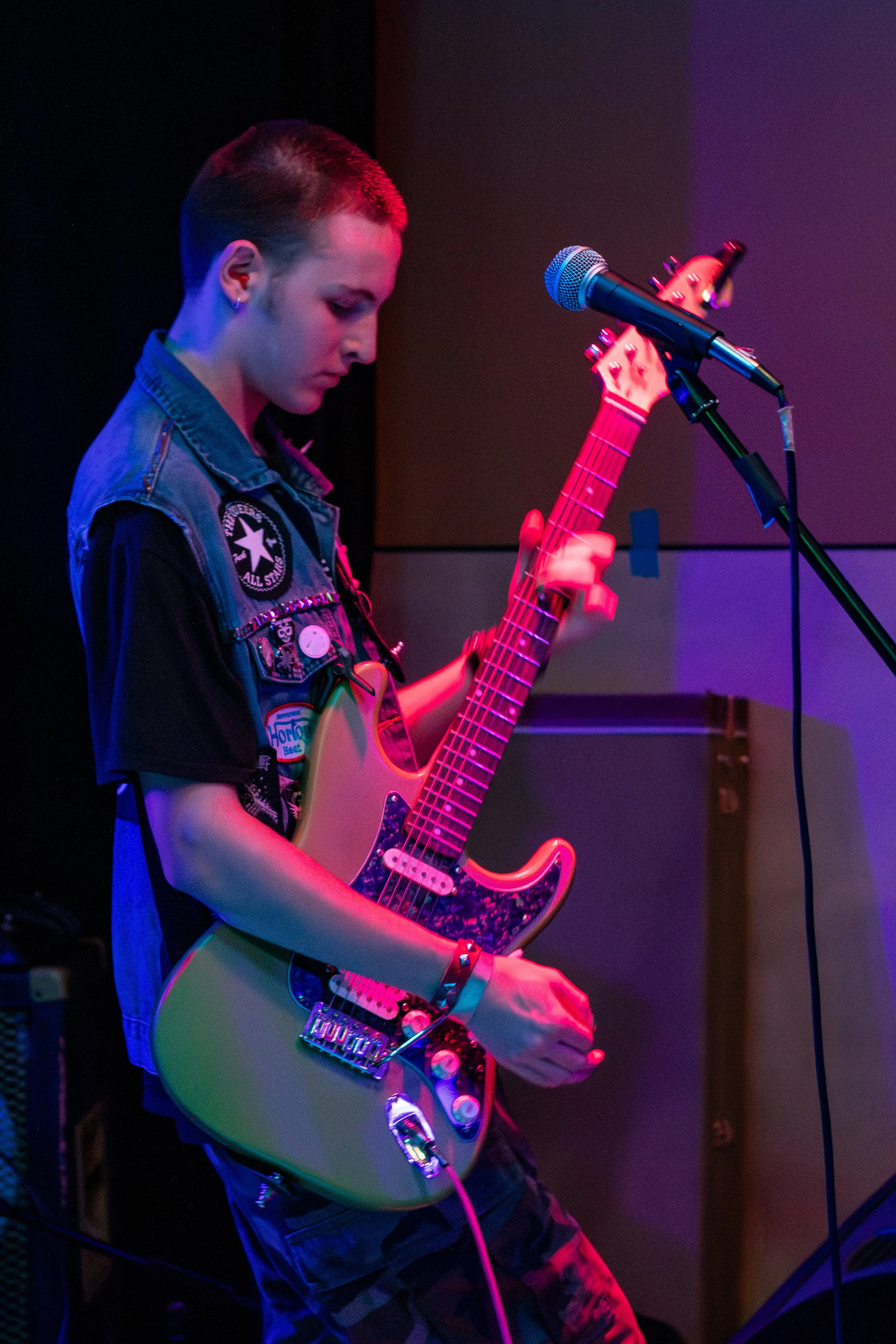 A young musician standing on stage, playing an electric guitar with colorful stage lighting.