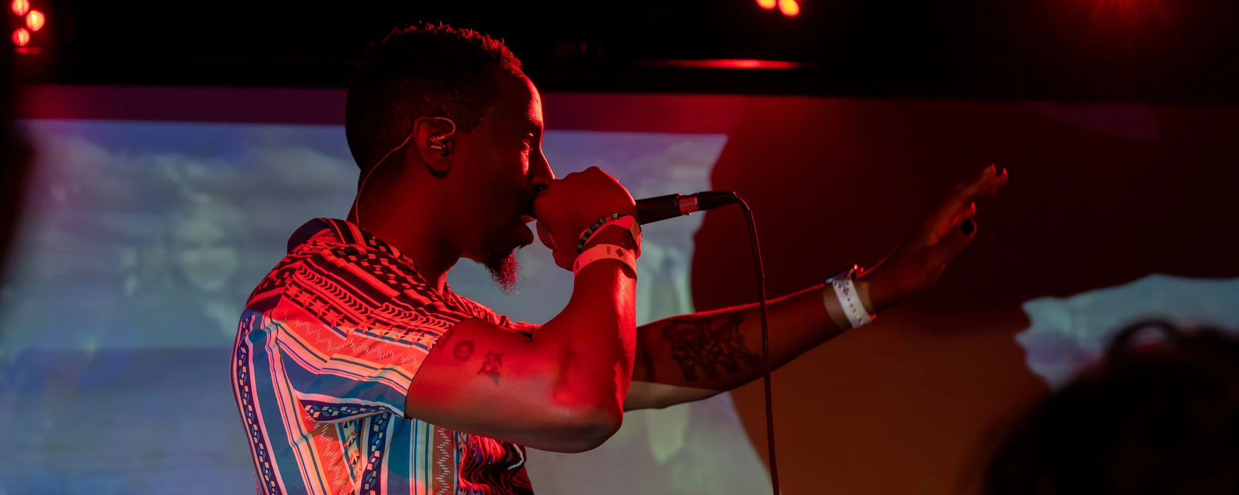A male performer singing into a microphone on stage with colorful lighting.