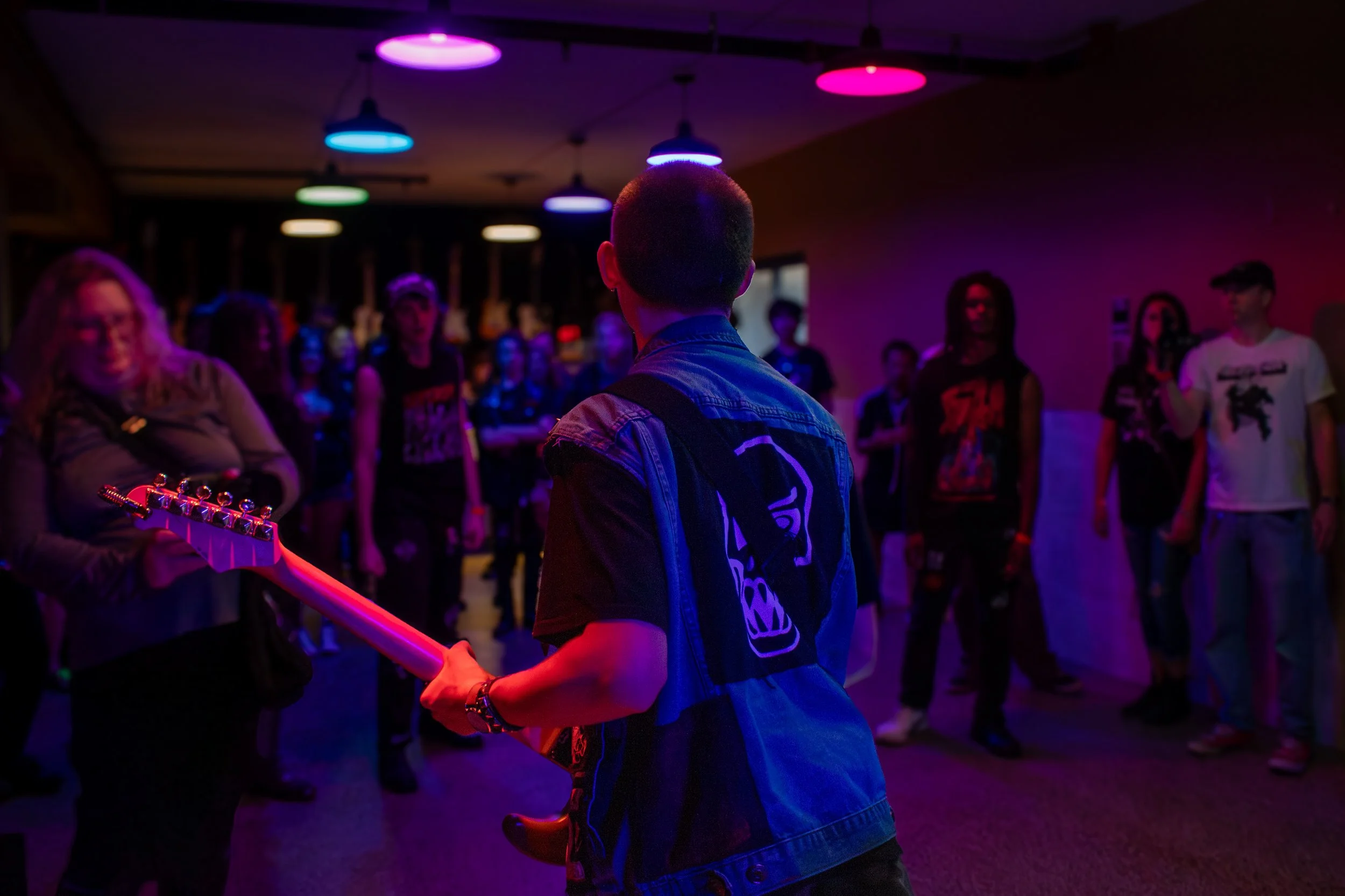 A person playing an electric guitar at a concert or party with a group of people watching, under colorful stage lights.