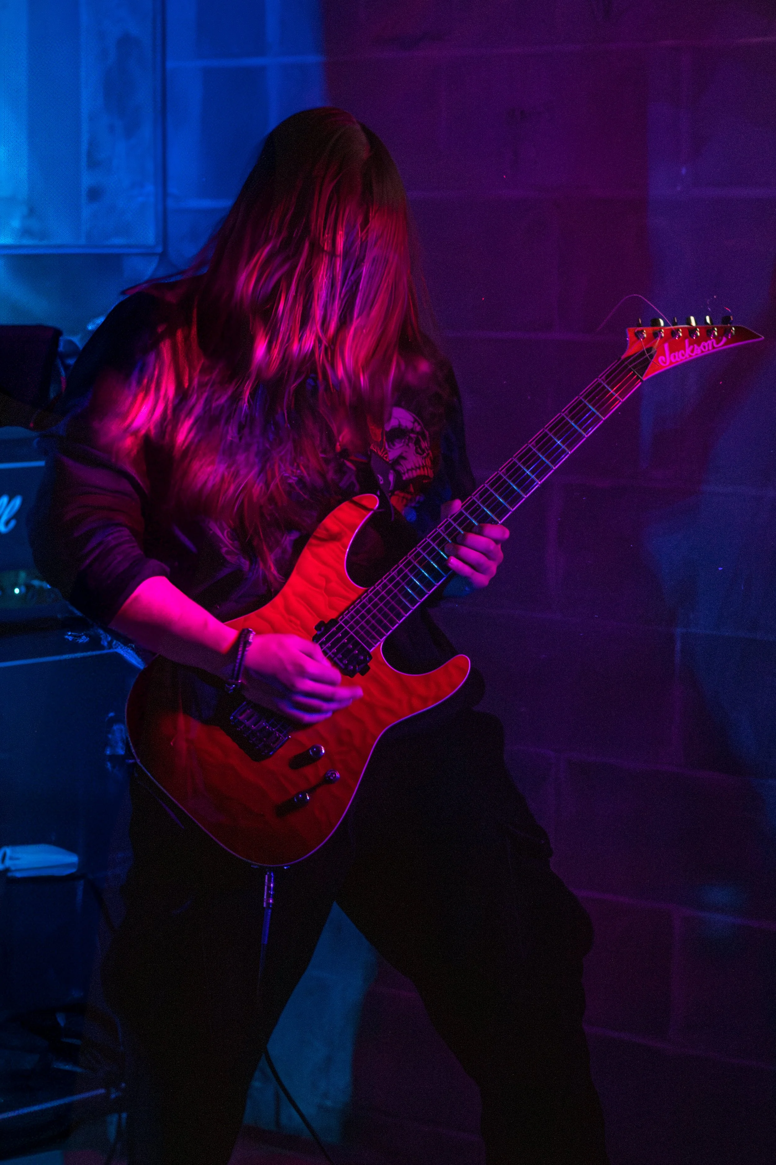 A person playing an electric guitar in a dimly lit room with colorful lighting.