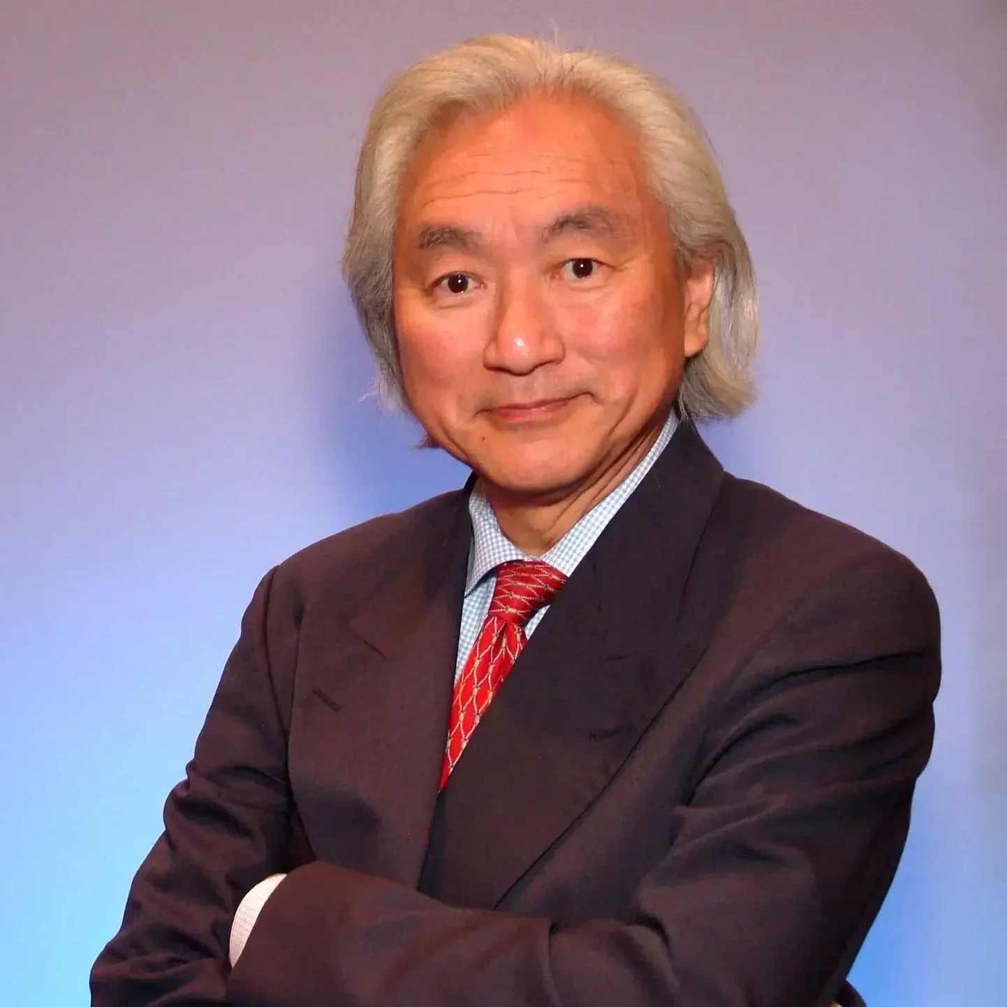Portrait of a middle-aged man with silver hair wearing a dark suit, white shirt, and red tie, crossed arms, smiling slightly, against a plain background.