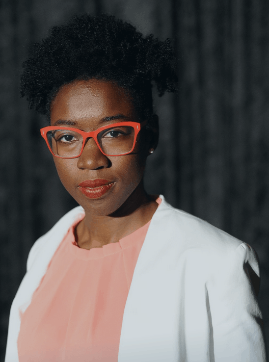 A professional portrait of Dr Joy Buolamwini, computer scientist and founder of the Algorithmic Justice League, smiling confidently. She is a leading expert on AI ethics and facial recognition bias.